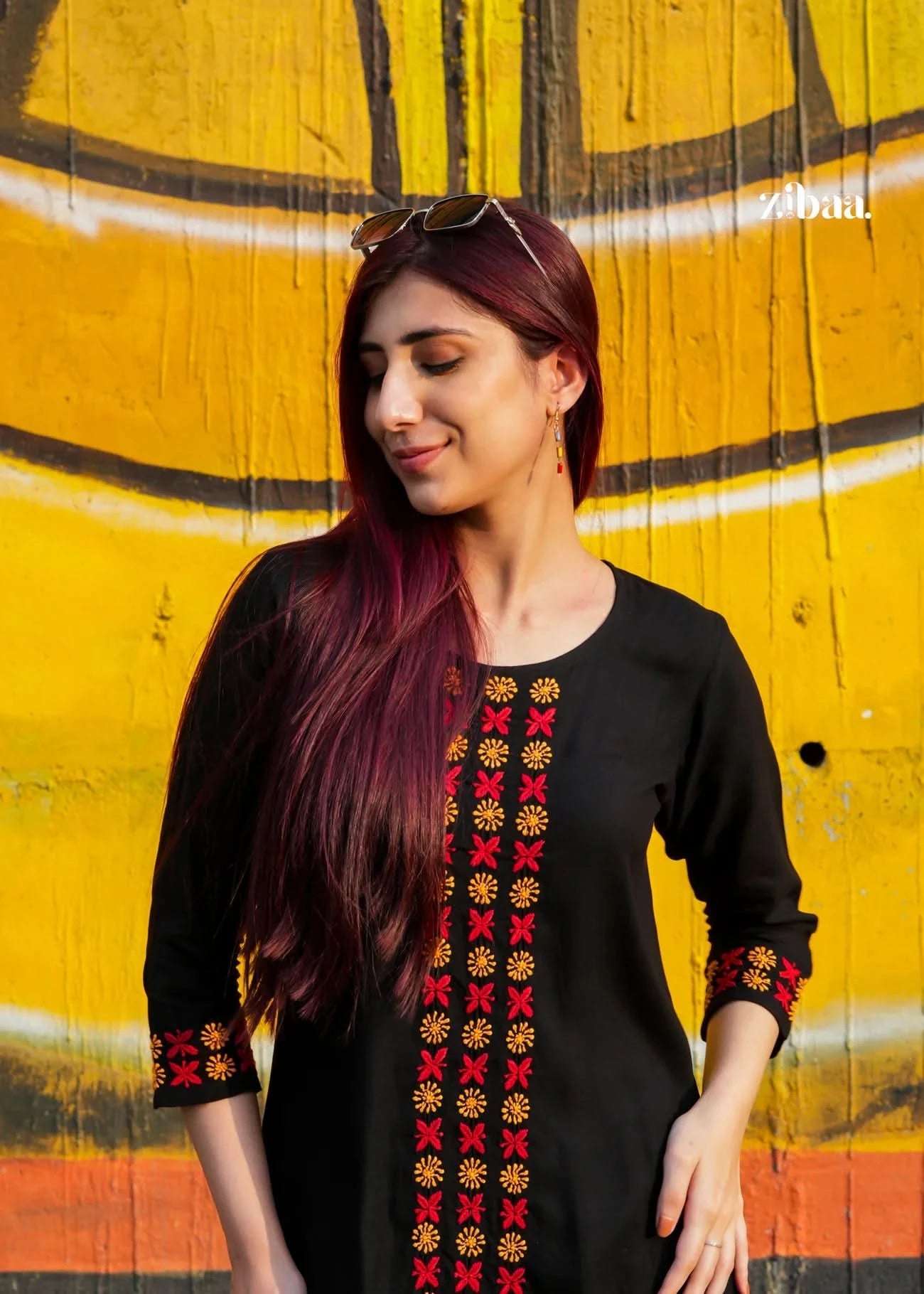 Woman wearing a black chikankari kurti set with colorful patterns against a yellow and orange background.