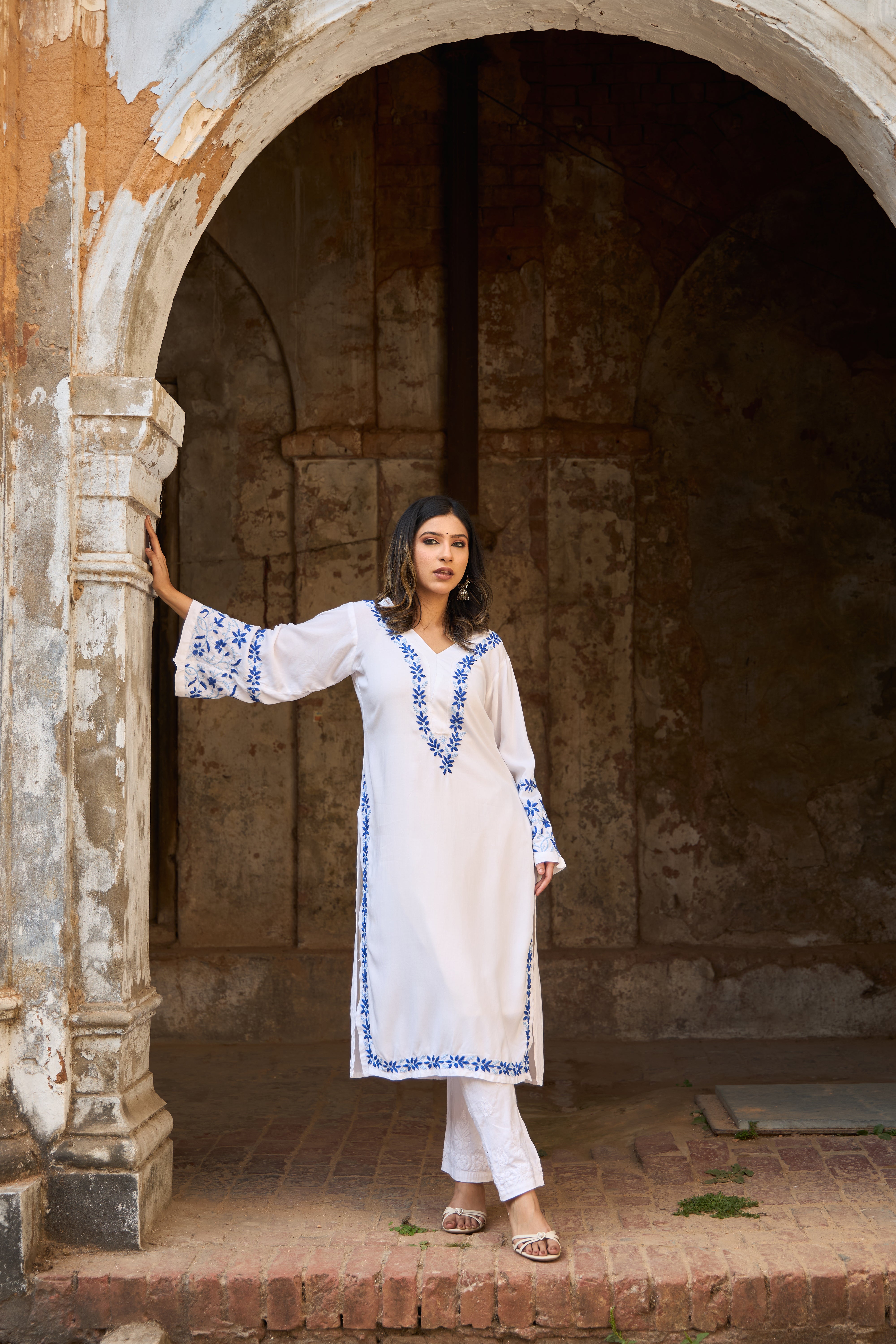 Woman in a White Chikankari Kurta  with blue embroidery standing in an arched doorway.