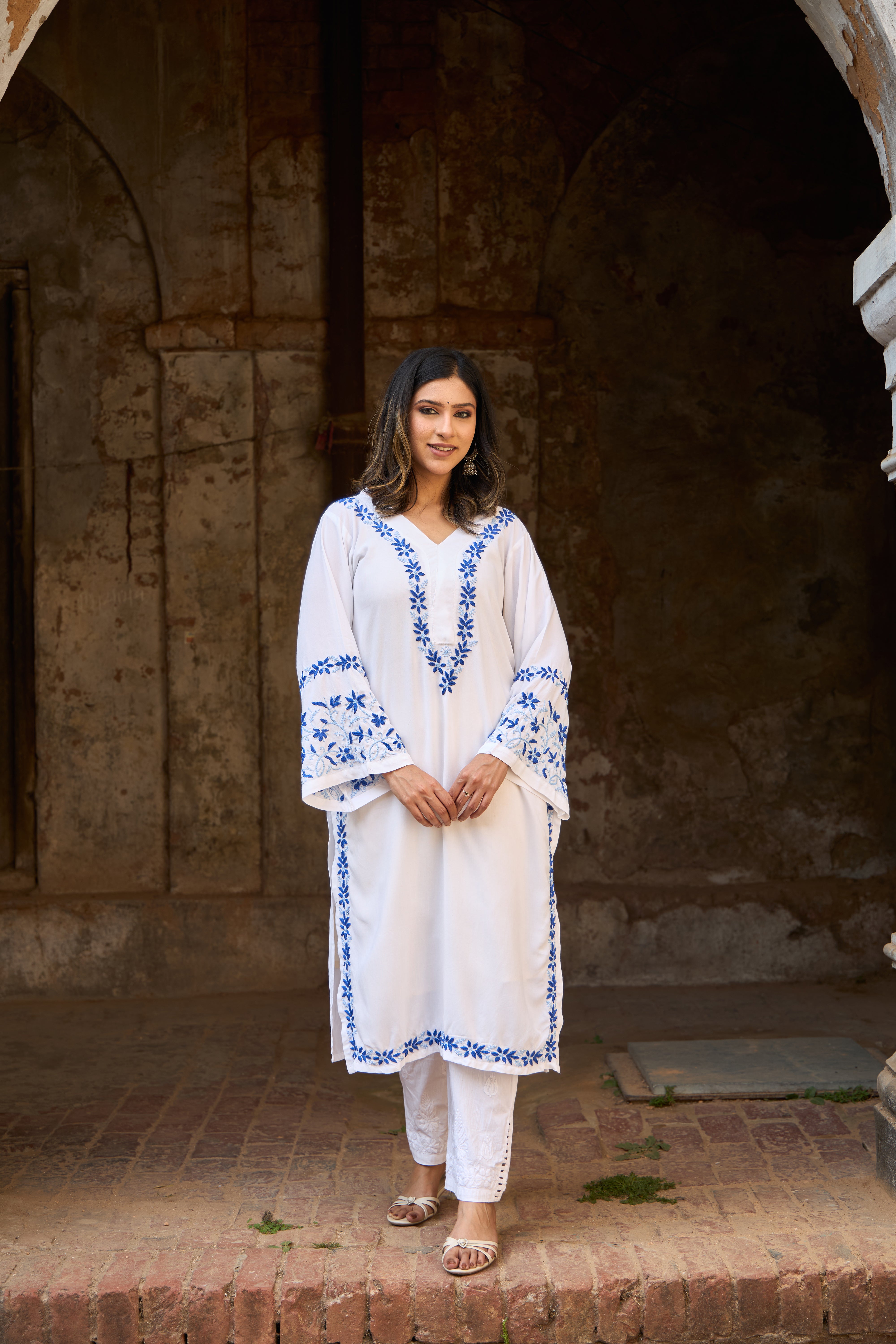 Woman in a white and blue Chikankari Kurta  standing in front of an archway.