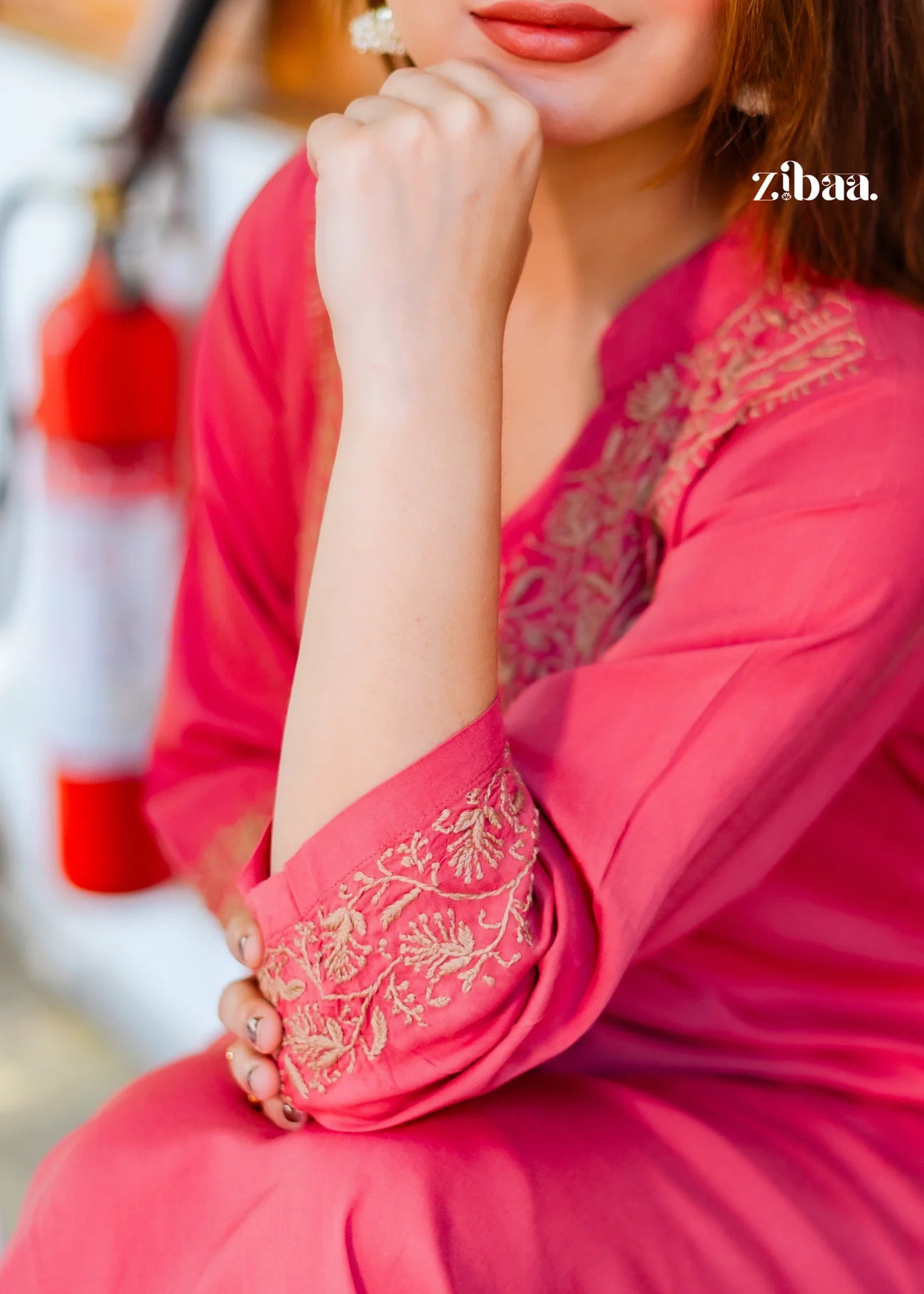 A close-up reveals the delicate golden embroidery threadwork on the cuffs and neckline of the coral chikankari kurti, showcasing the beautiful detail and fine stitching..