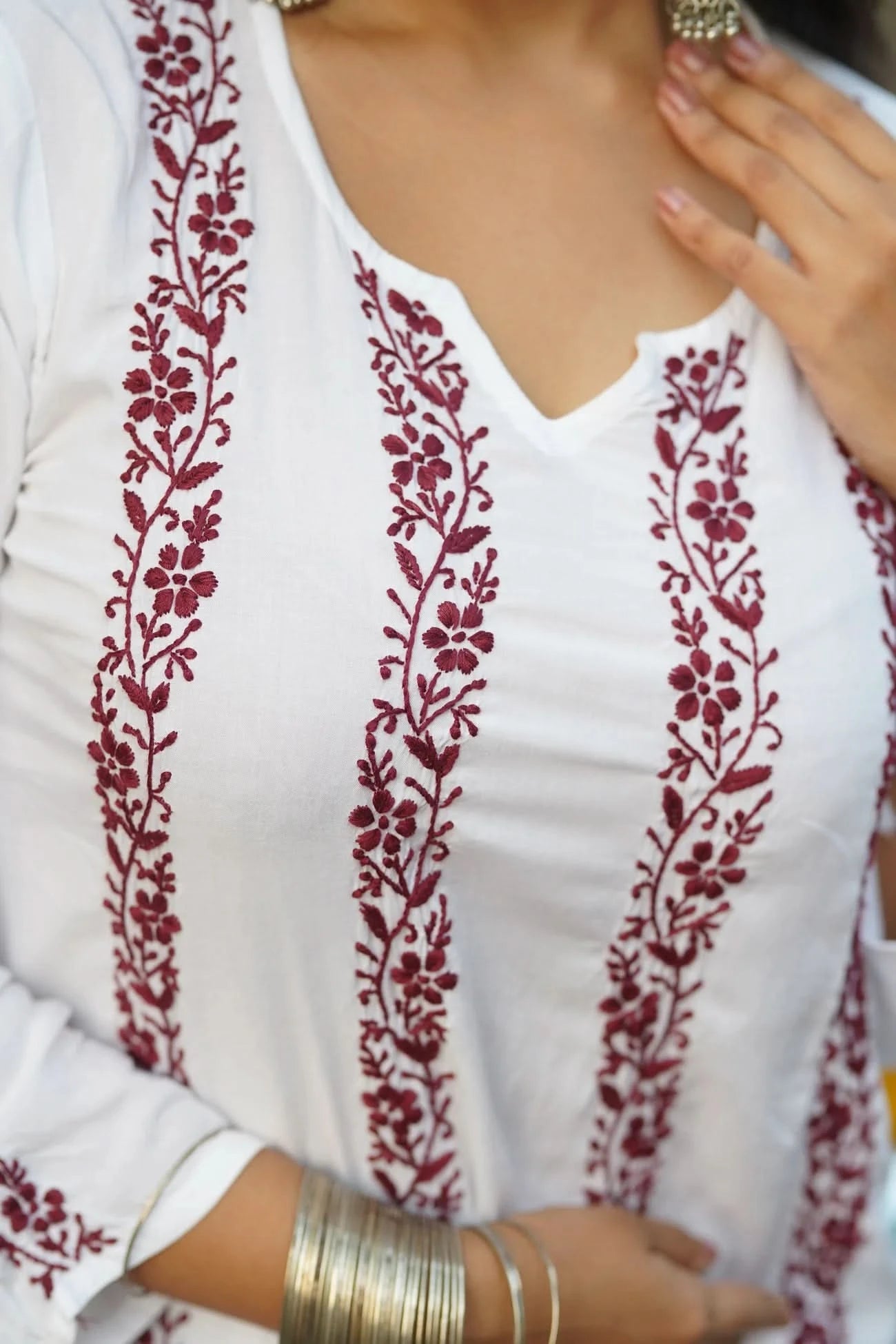 White top with red floral embroidery worn by a person.