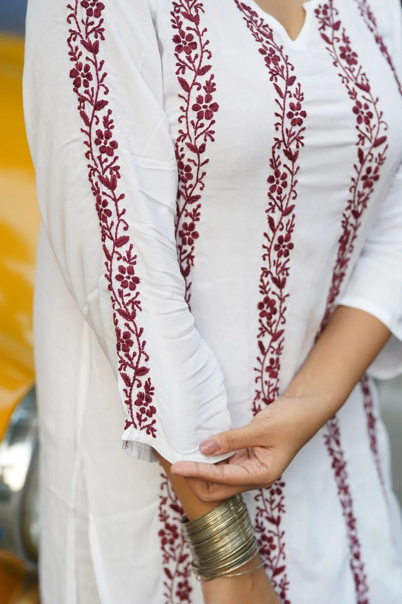 White garment with red floral embroidery held by a person wearing a gold bracelet.