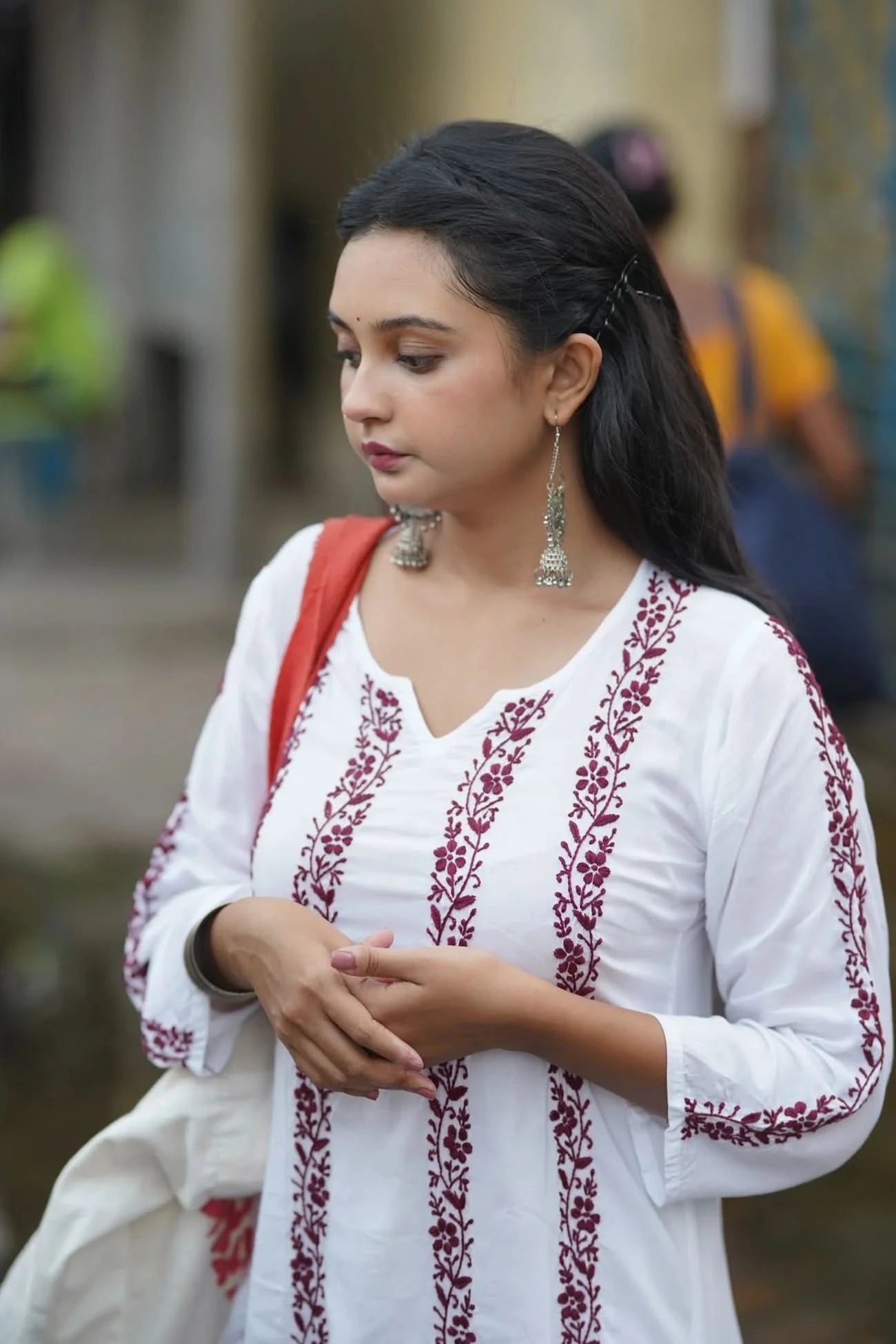 Woman wearing a white embroidered top with red patterns, holding a white bag.