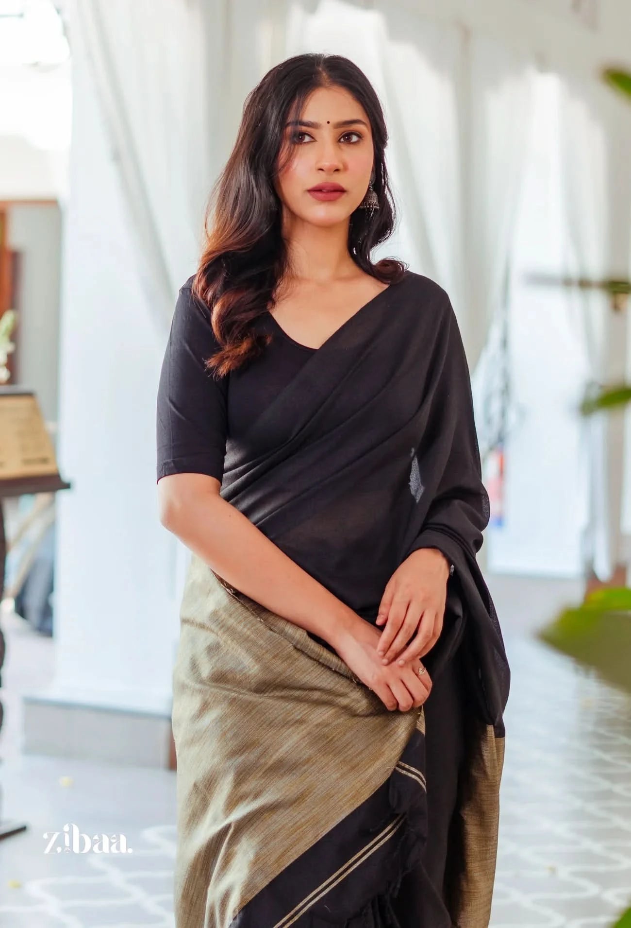 Woman wearing a black top and green saree with a blurred indoor background