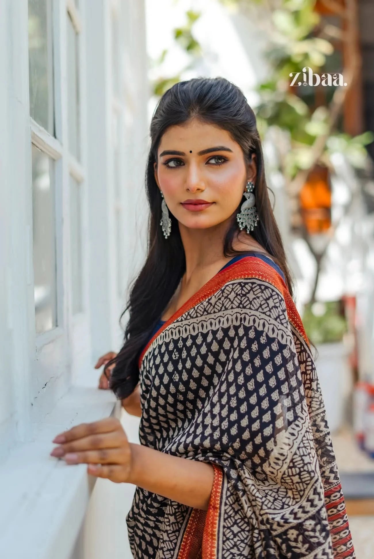 Woman wearing a patterned saree with a blurred outdoor background