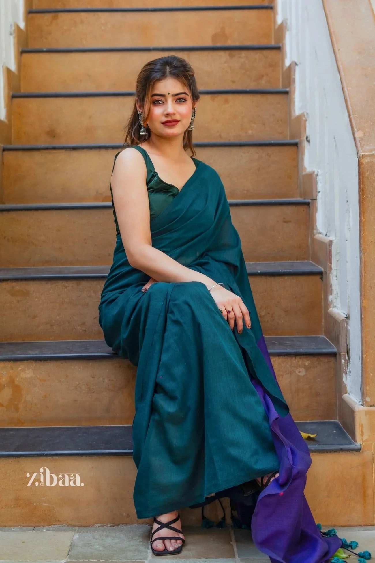 Woman in a teal saree sitting on a staircase