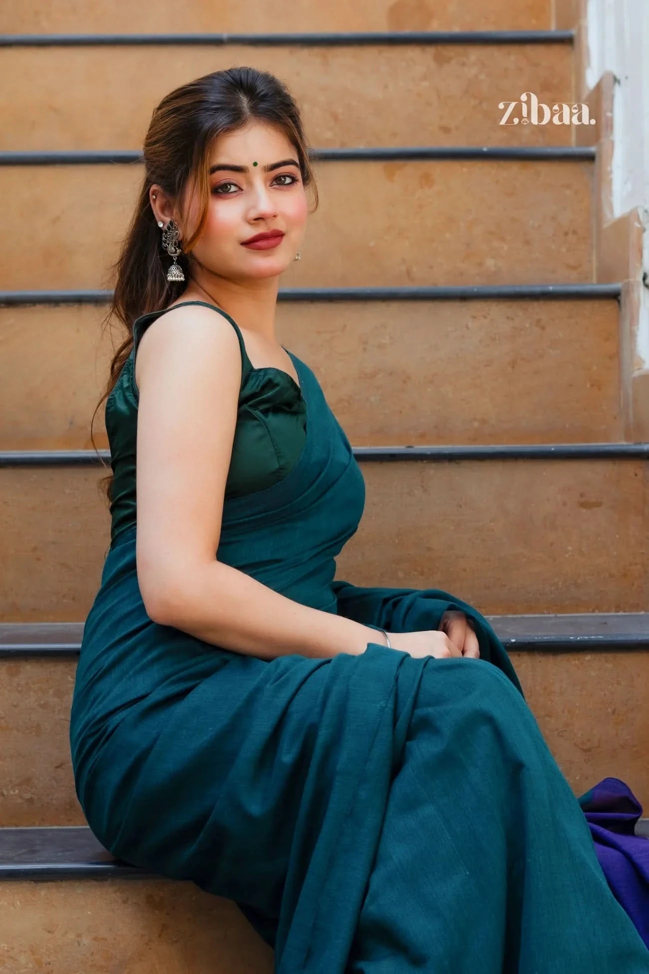 Woman in a teal dress sitting on steps with 'zibaa' branding.
