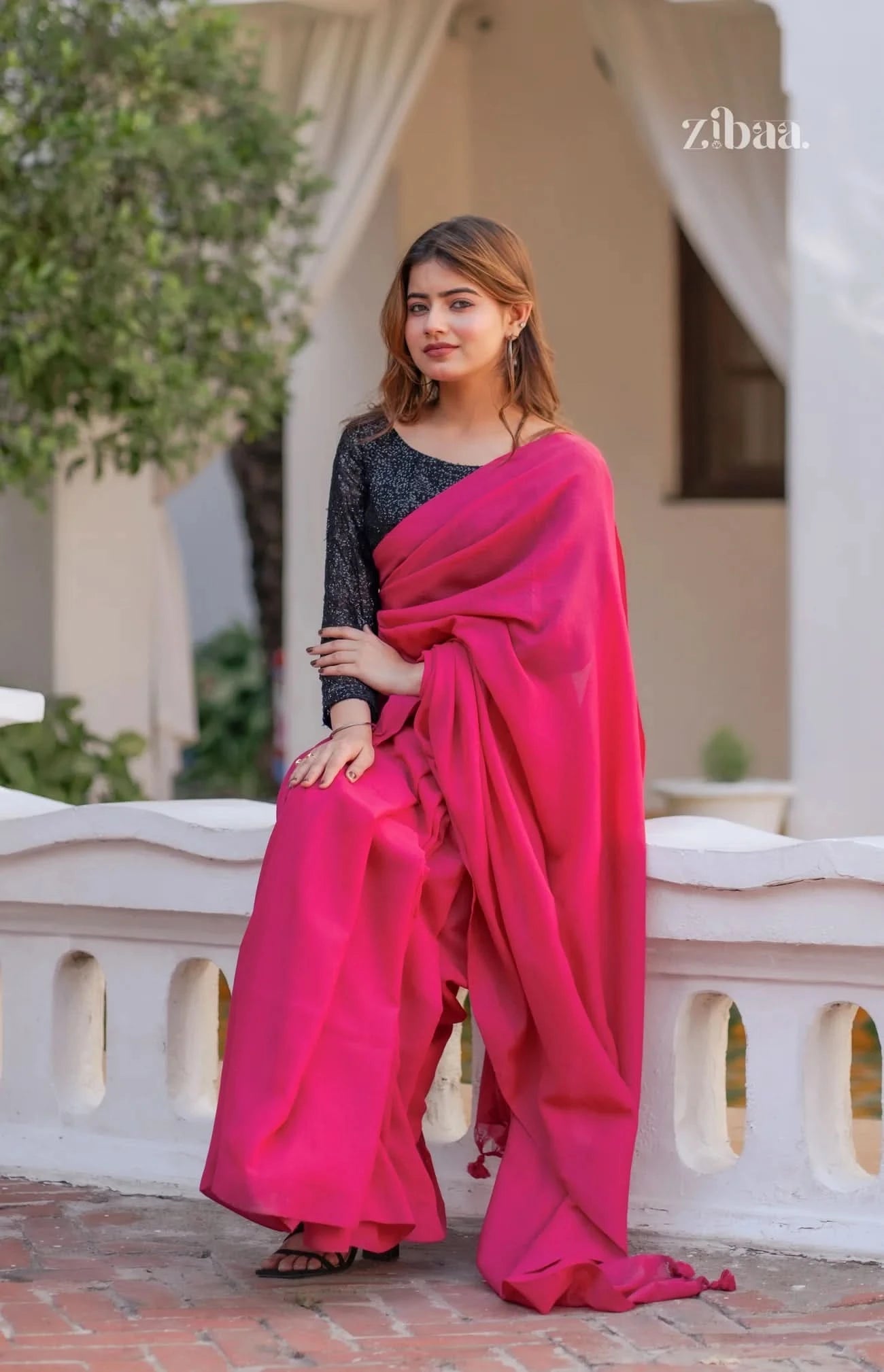 Woman wearing a bright pink saree with a black blouse, standing outdoors.