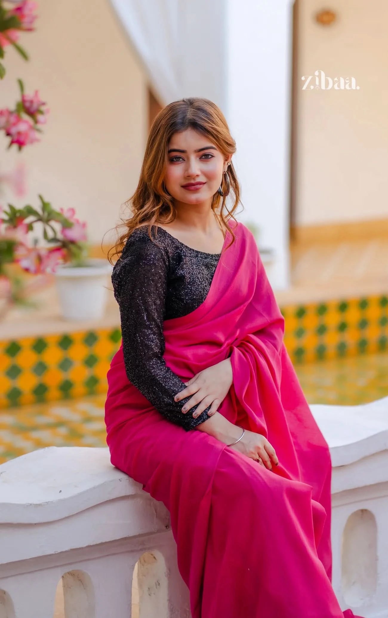 Woman in a pink saree with a black blouse sitting on a ledge with a blurred background