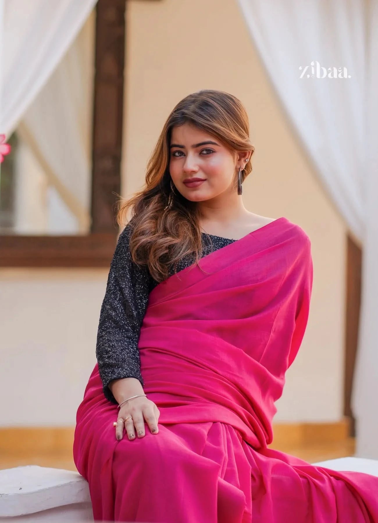 Woman in a pink saree sitting indoors with a blurred background