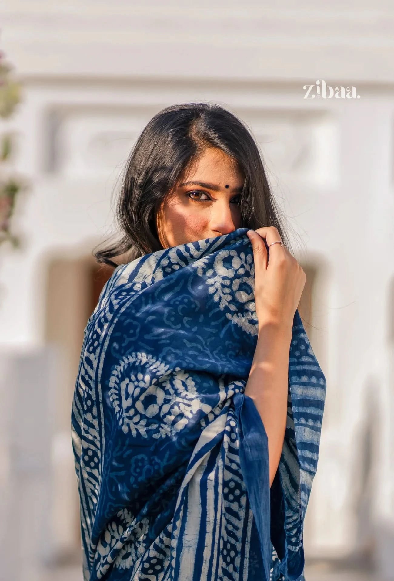 Woman wearing a blue and white patterned shawl, with 'zibaa' branding visible.