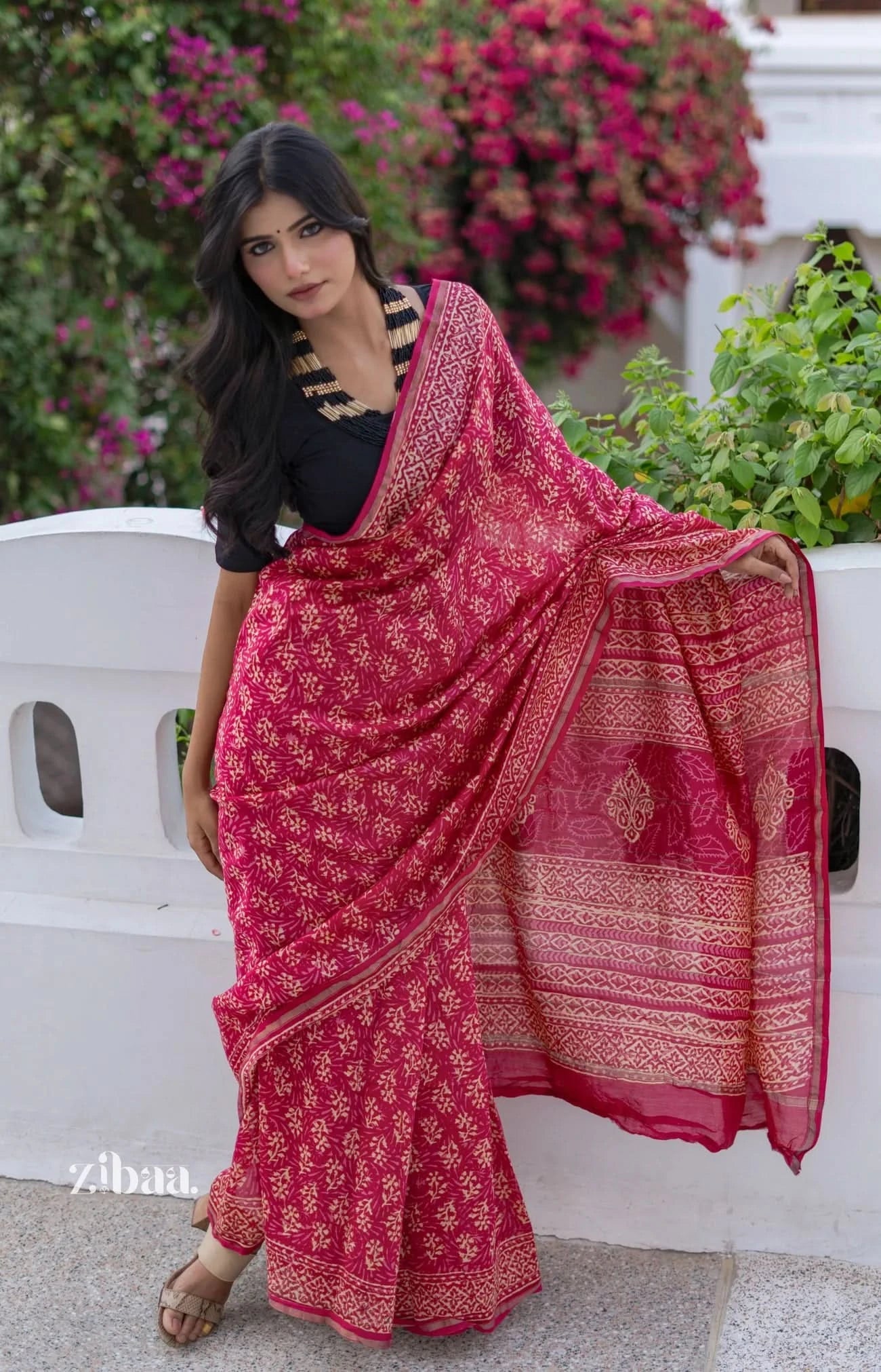 Woman wearing a red saree with a white background and floral decorations.