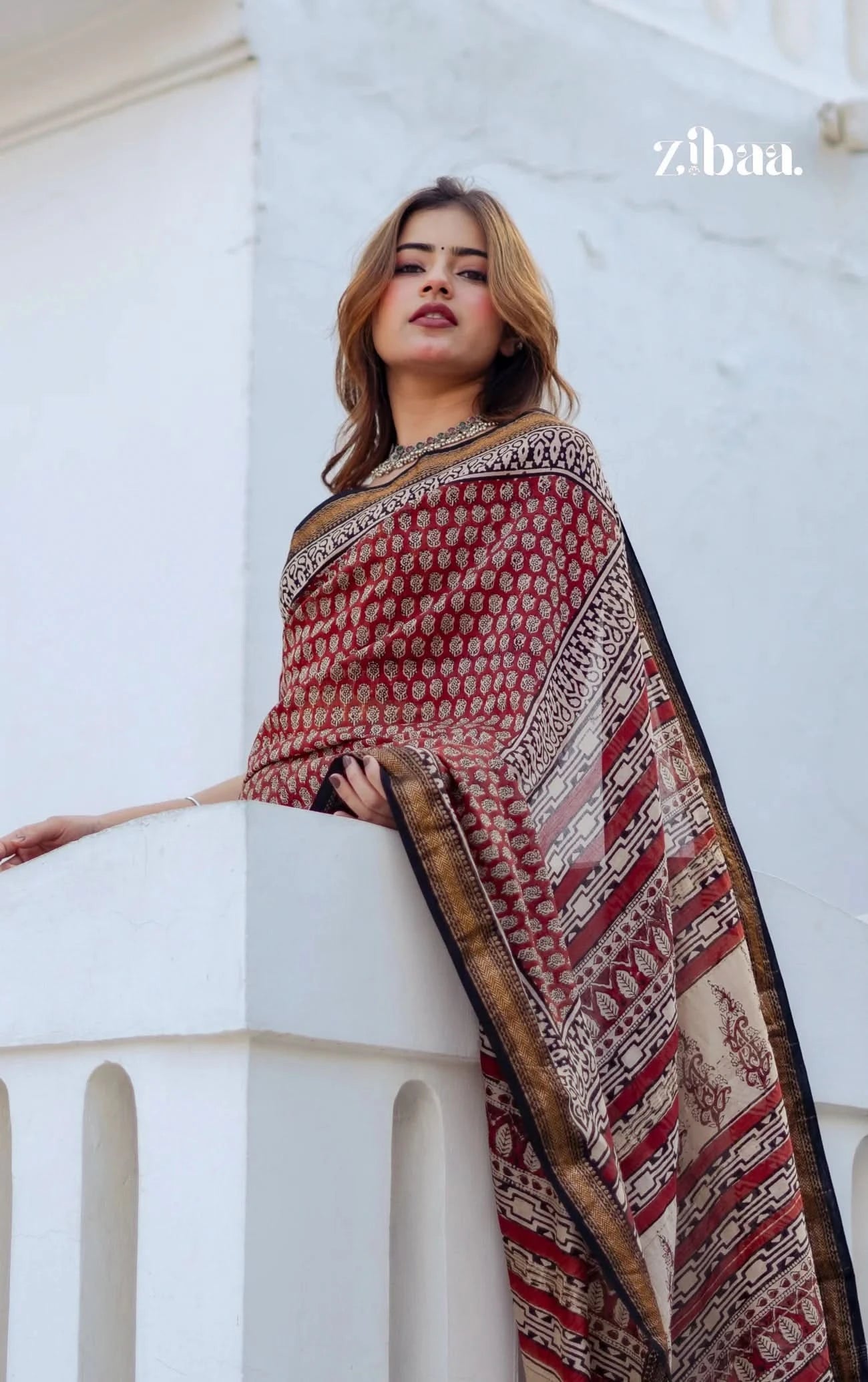 Woman wearing a patterned shawl on a white architectural background with 'zibaa' branding.