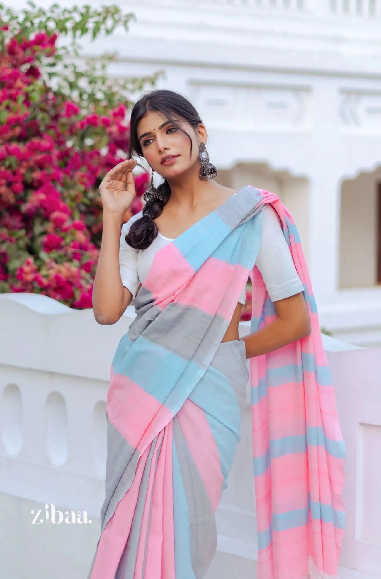 Woman wearing a colorful saree with a blurred background of pink flowers and a white building.