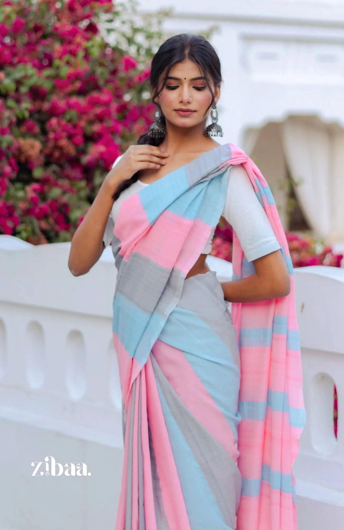 Woman wearing a pink and gray saree with a blurred floral background
