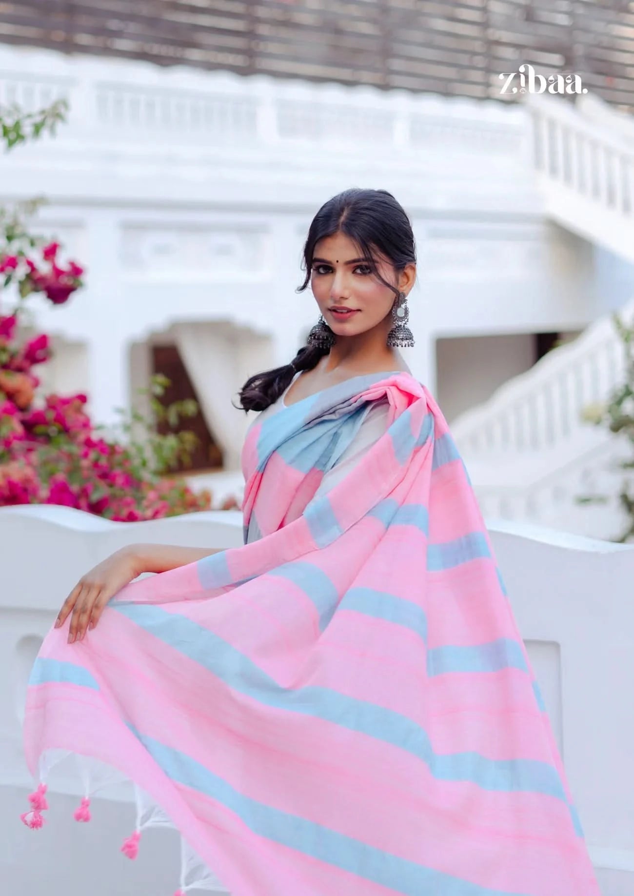 Woman wearing a pink and gray striped saree with floral decorations, standing outdoors.