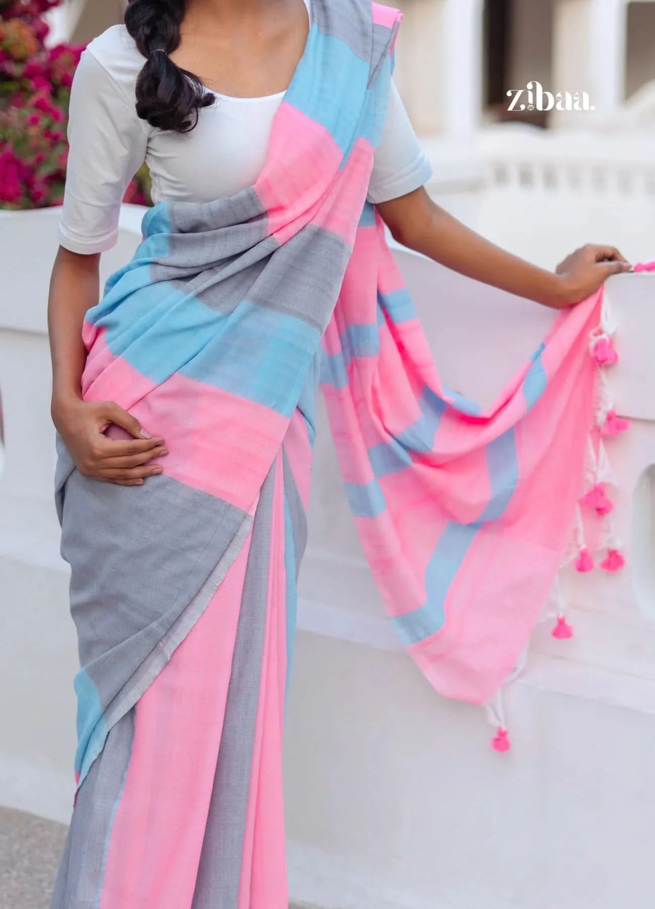 Woman wearing a colorful saree with pink, gray, and blue patterns, holding it up.