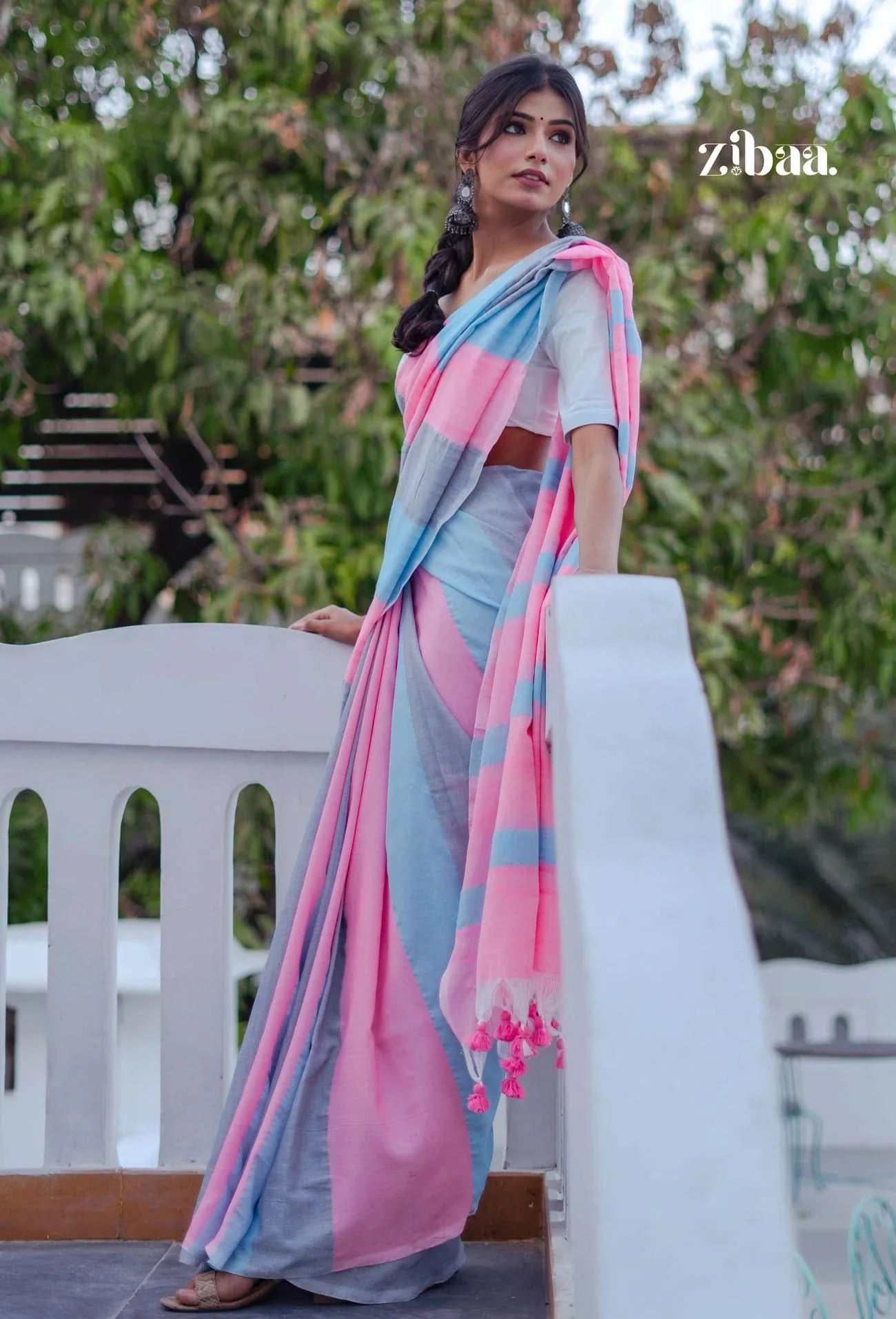 Woman in a light blue saree with pink and gray accents standing outdoors.