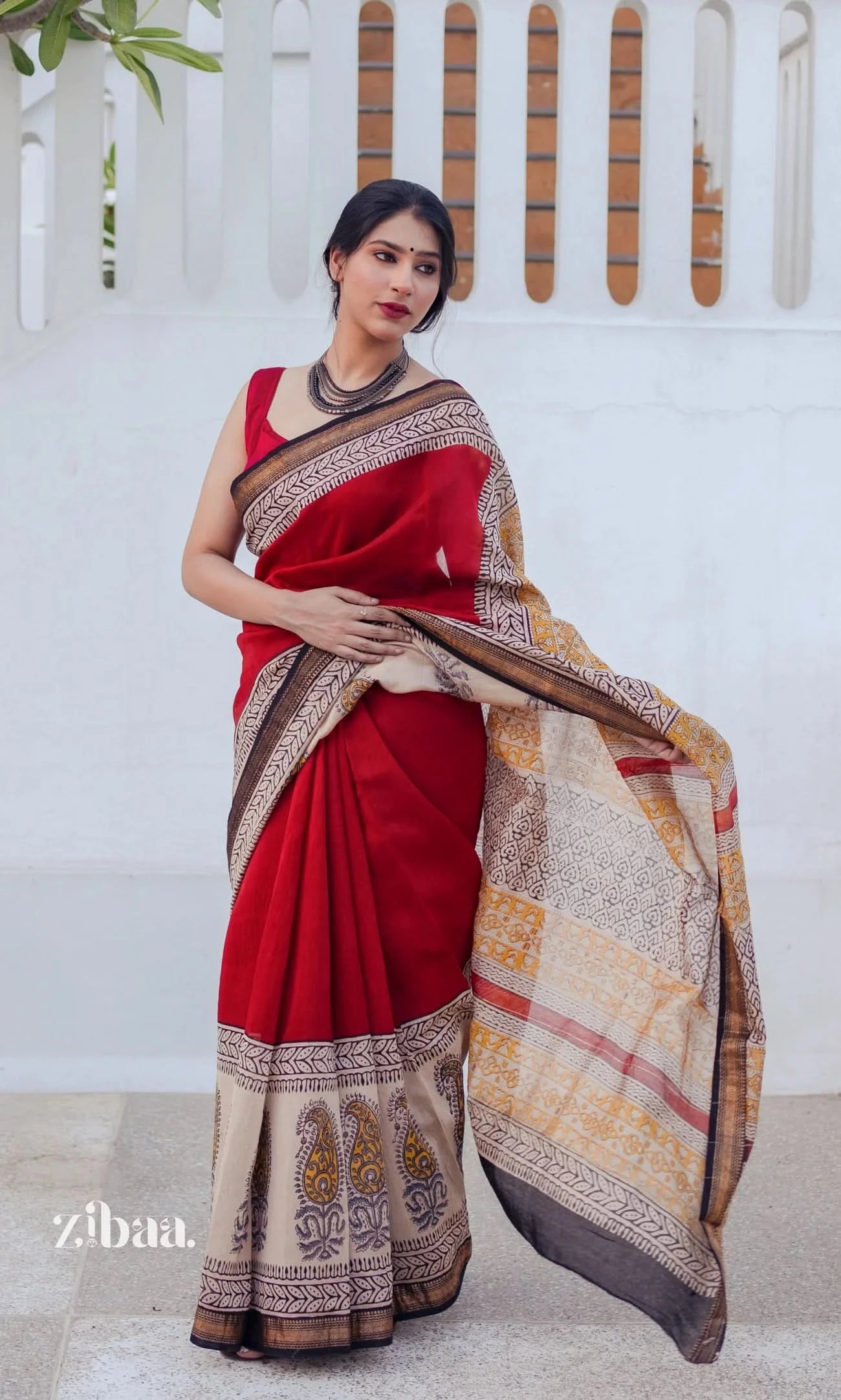 Woman wearing a red saree with a patterned border against a white background