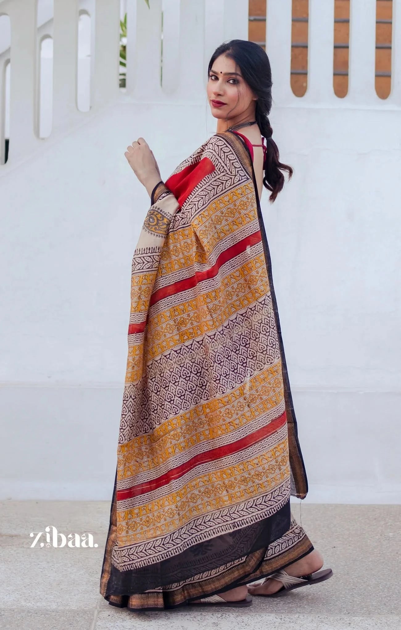 Woman wearing a traditional saree with a white background, featuring the brand 'zibaa'.