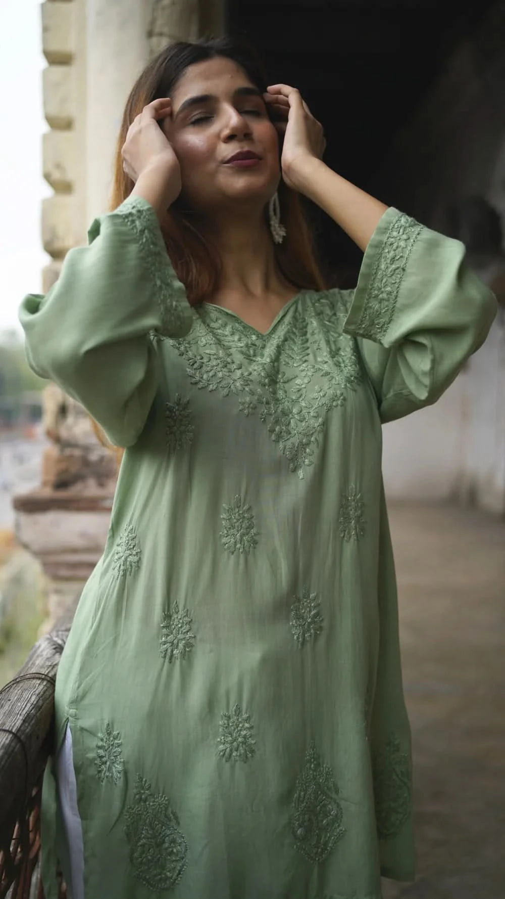 Woman wearing a light green embroidered dress standing outdoors.