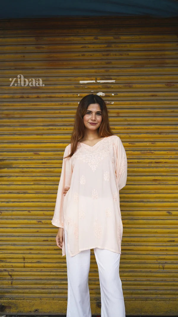 Woman wearing a light pink top and white pants standing in front of a yellow shutter with 'zibaa' branding.