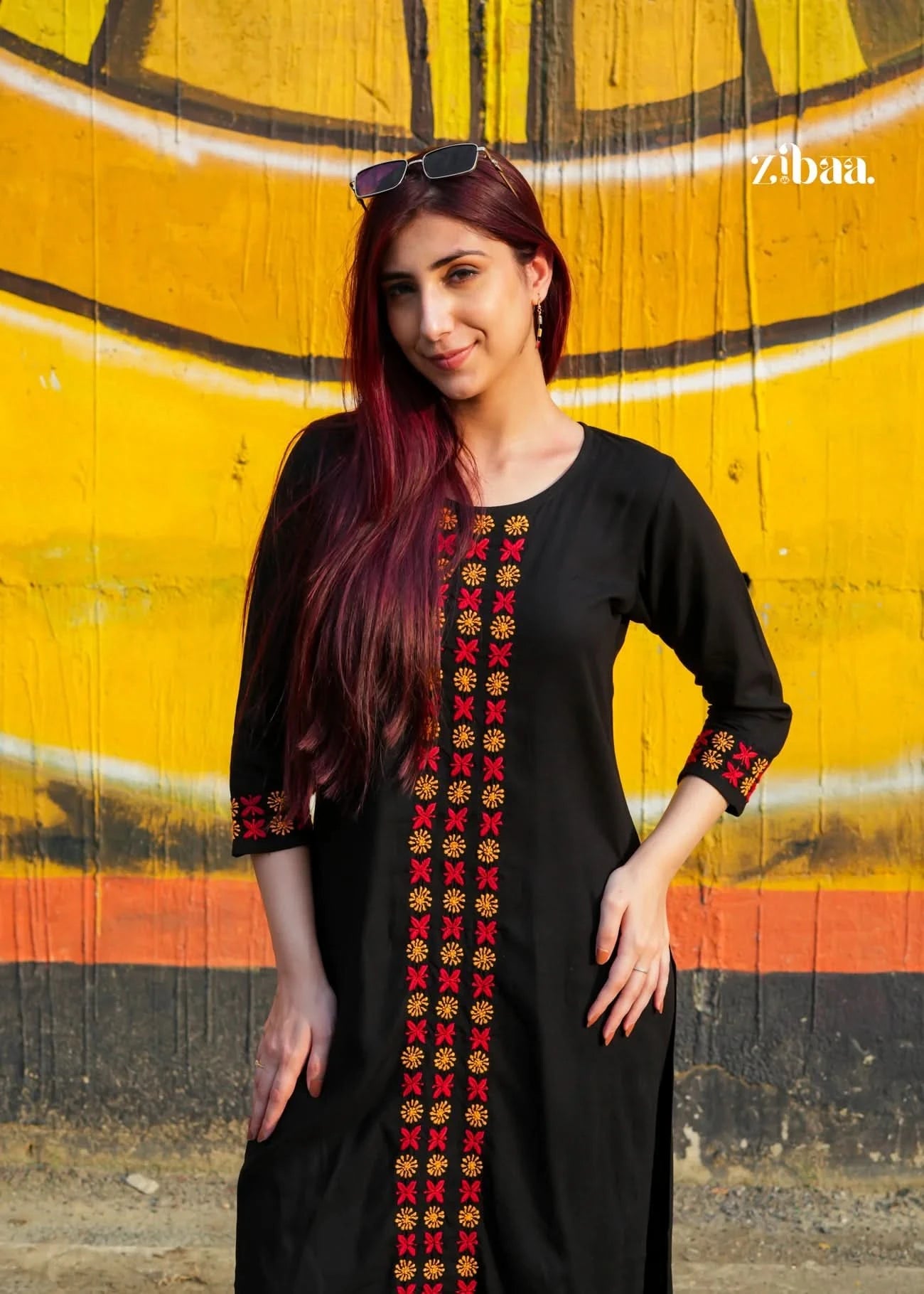 Woman wearing a black chikankari kurti set with colorful embroidery against a yellow and orange wall.