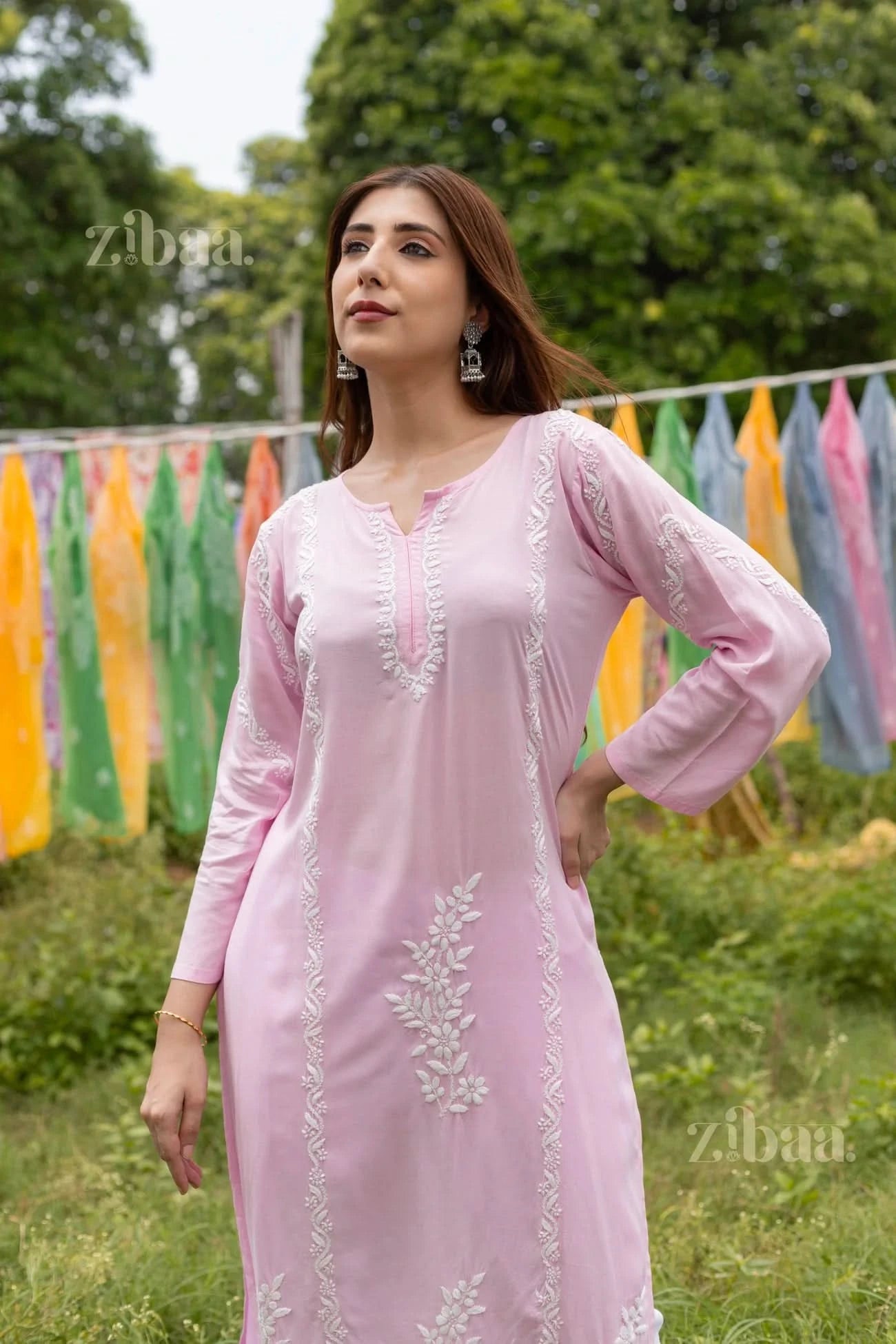 Girl draped in a beautiful white churidaar and a pink chikankari kurta, posing in an exotic outdoor setting with brilliant drapes.
