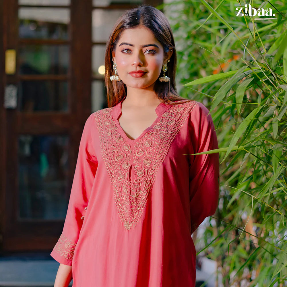 Woman wearing a pink embroidered dress standing outdoors with greenery in the background