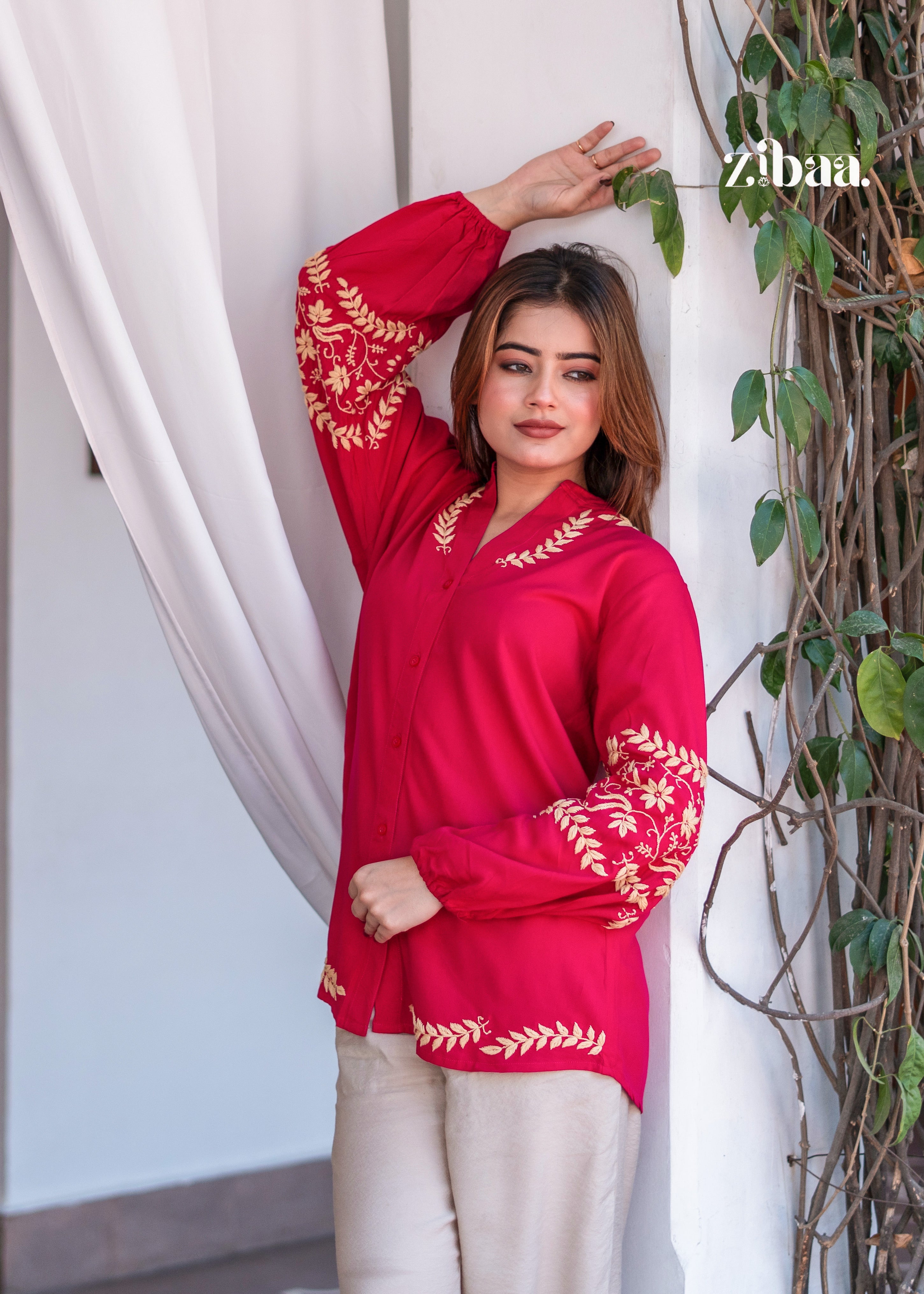 he model is wearing a hot pink embroidered kurta with beige pants. Hot Pink Embroidered Kurta with Beige Pants features intricate golden threadwork on the sleeves and neckline. She poses gracefully near a curtain, highlighting the elegant ethnic wear.
