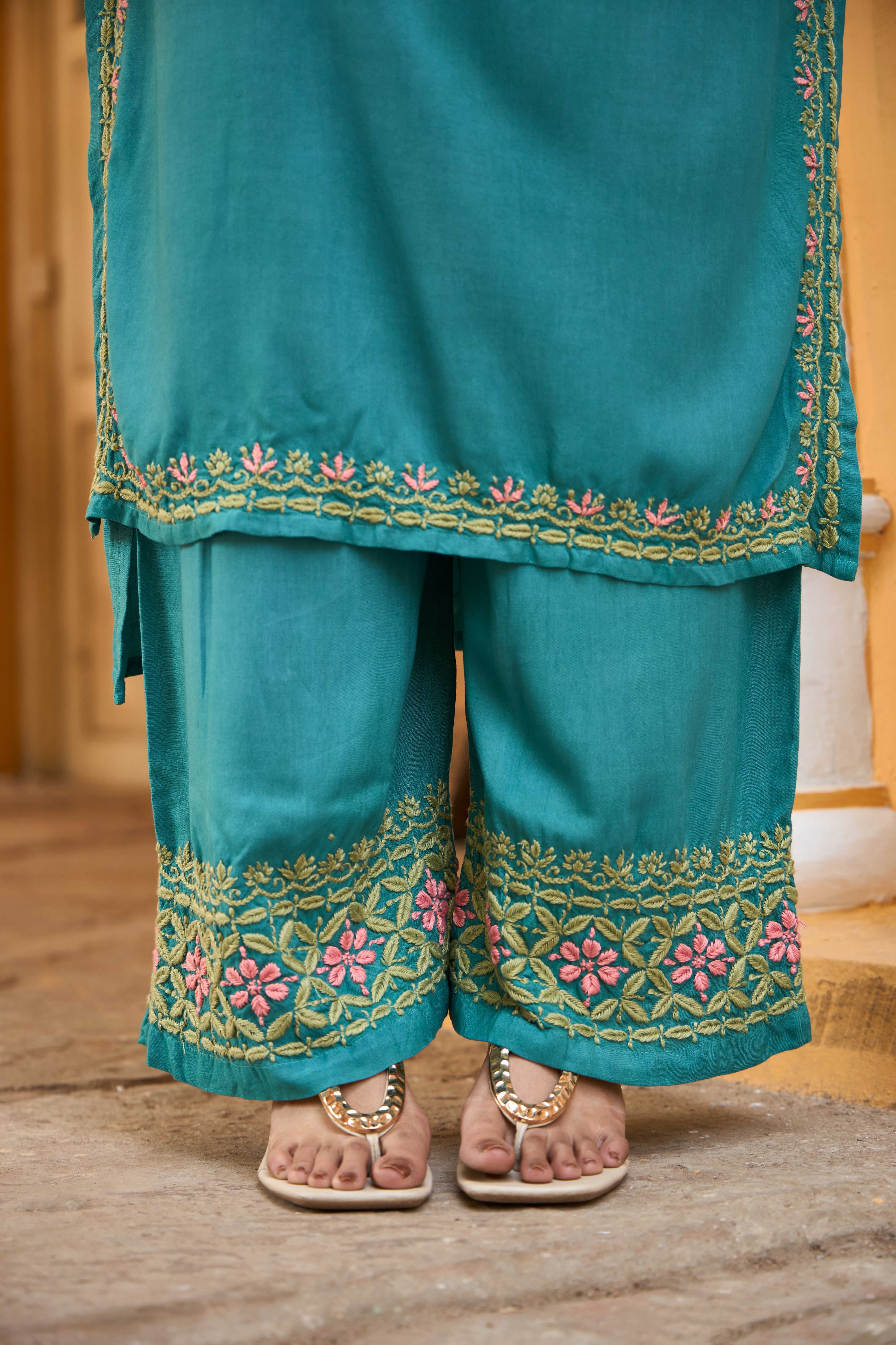 Teal traditional chikankari set with floral embroidery on a wooden floor.