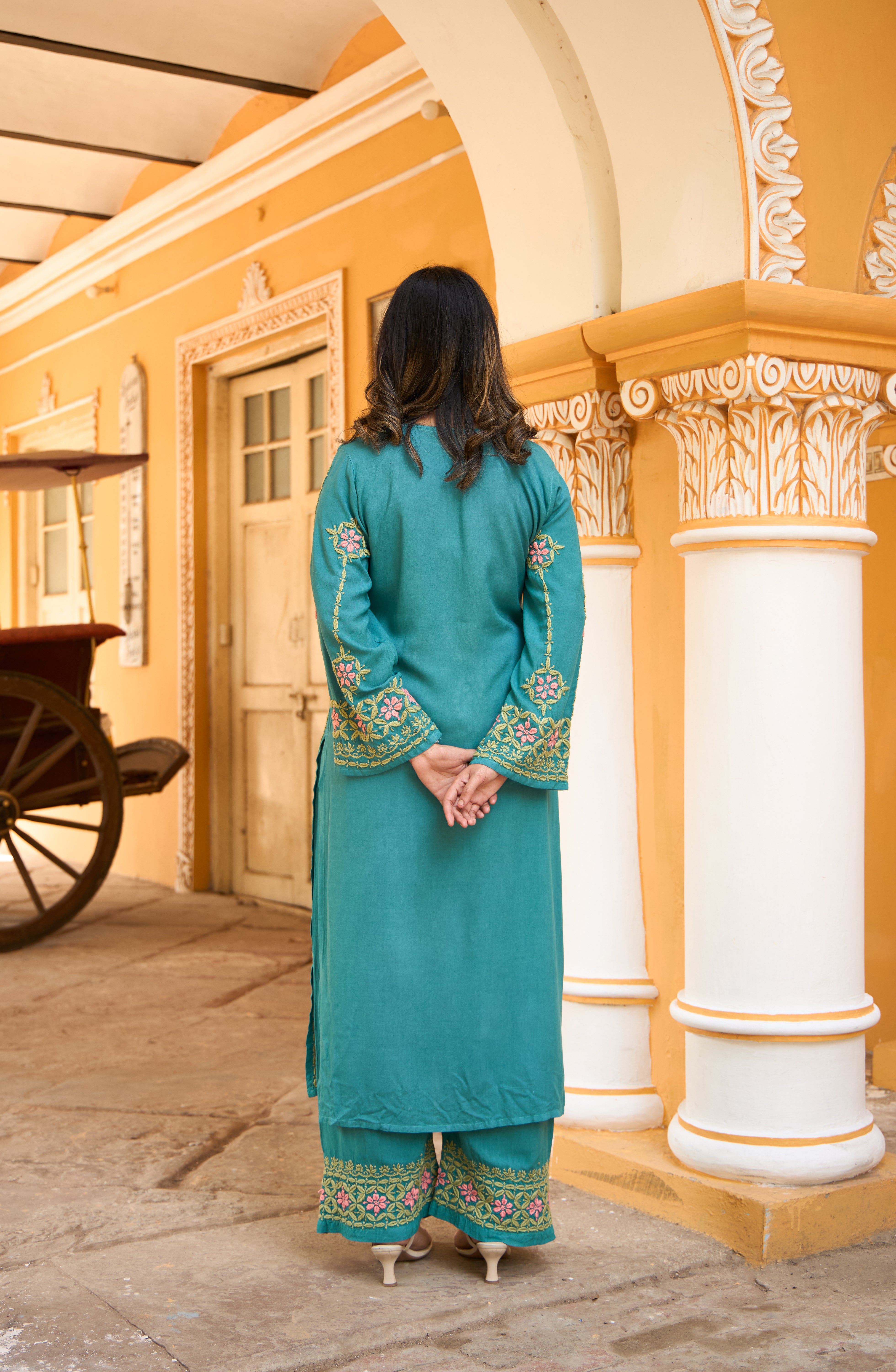 Woman in a turquoise traditional Chikankari kurta set standing in front of an ornate building.