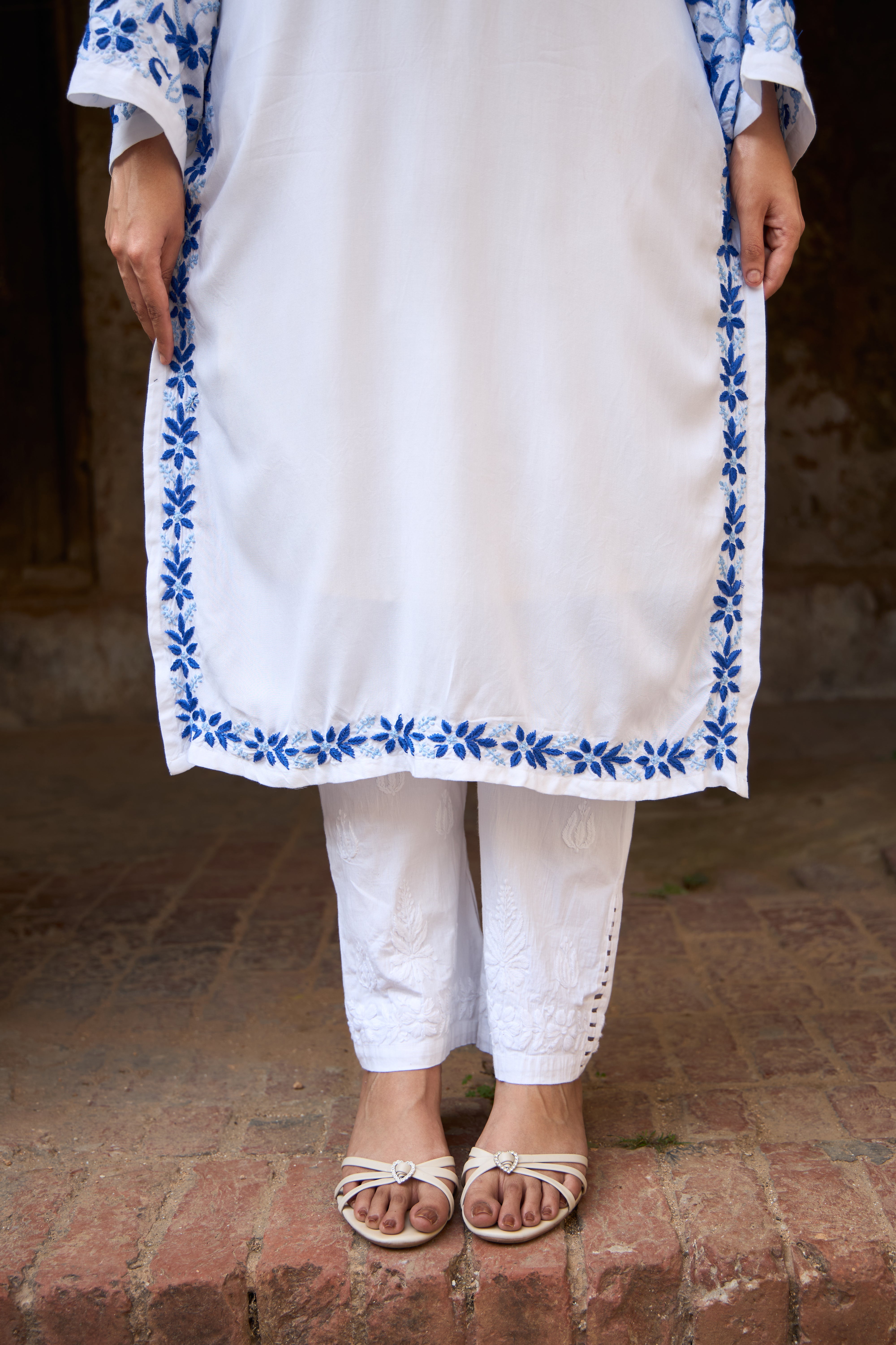White Chikankari Kurta with blue embroidery on a textured floor.