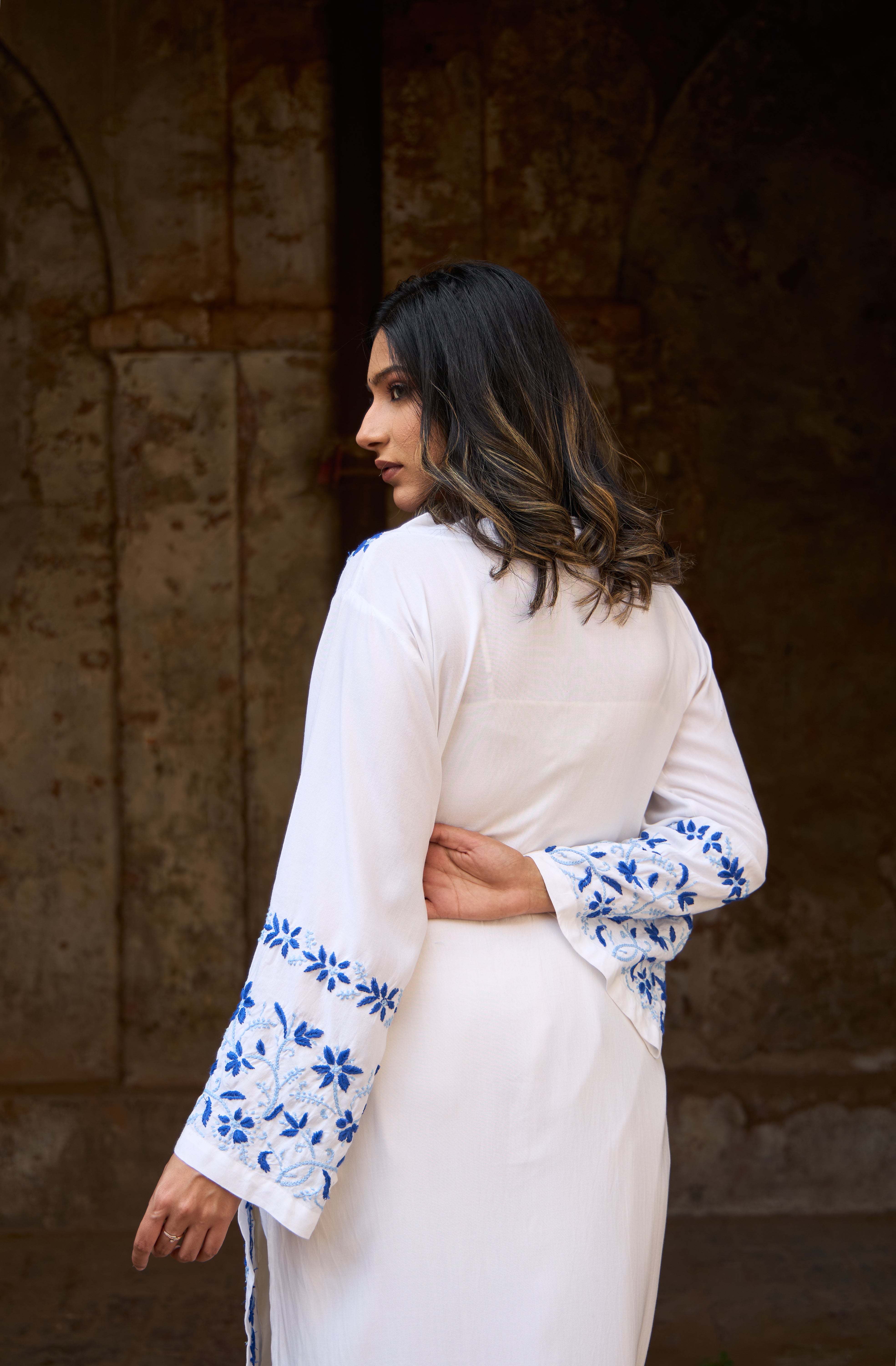 Woman wearing a White Chikankari Kurta with blue floral patterns in a dimly lit setting
