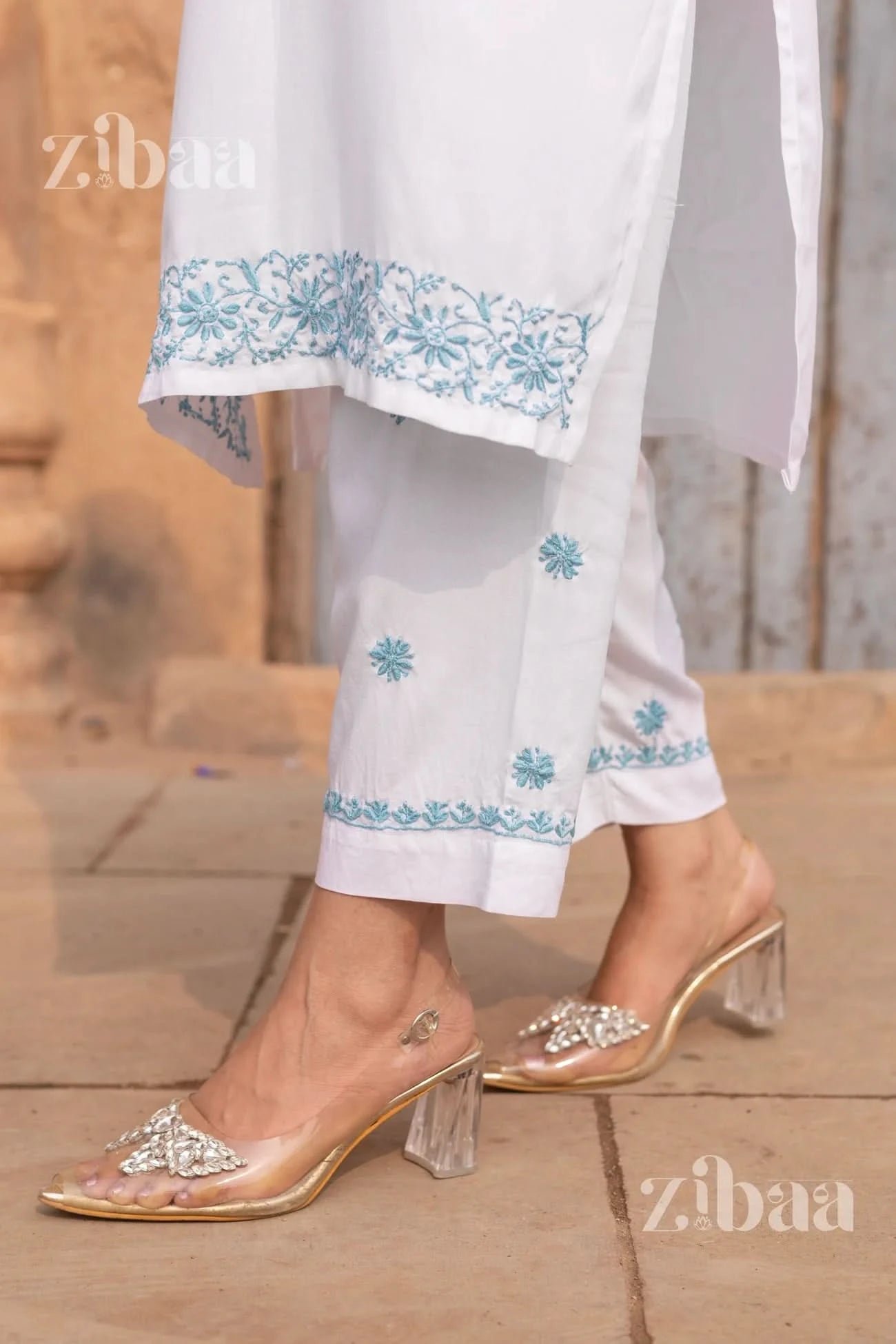 White outfit with blue floral embroidery and clear high-heeled sandals on a blurred background