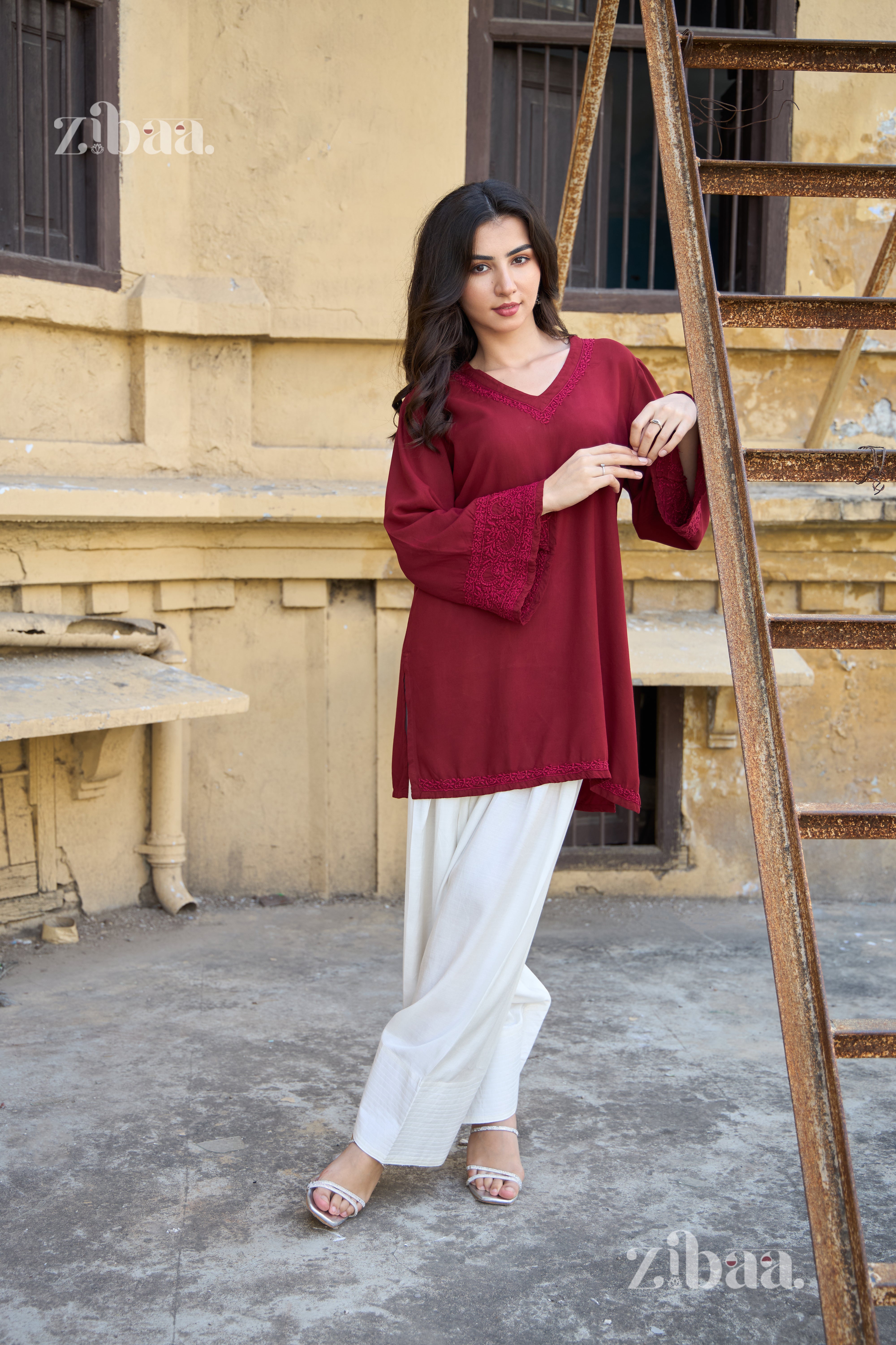 Woman in a red top and white pants standing next to a ladder against a beige wall.