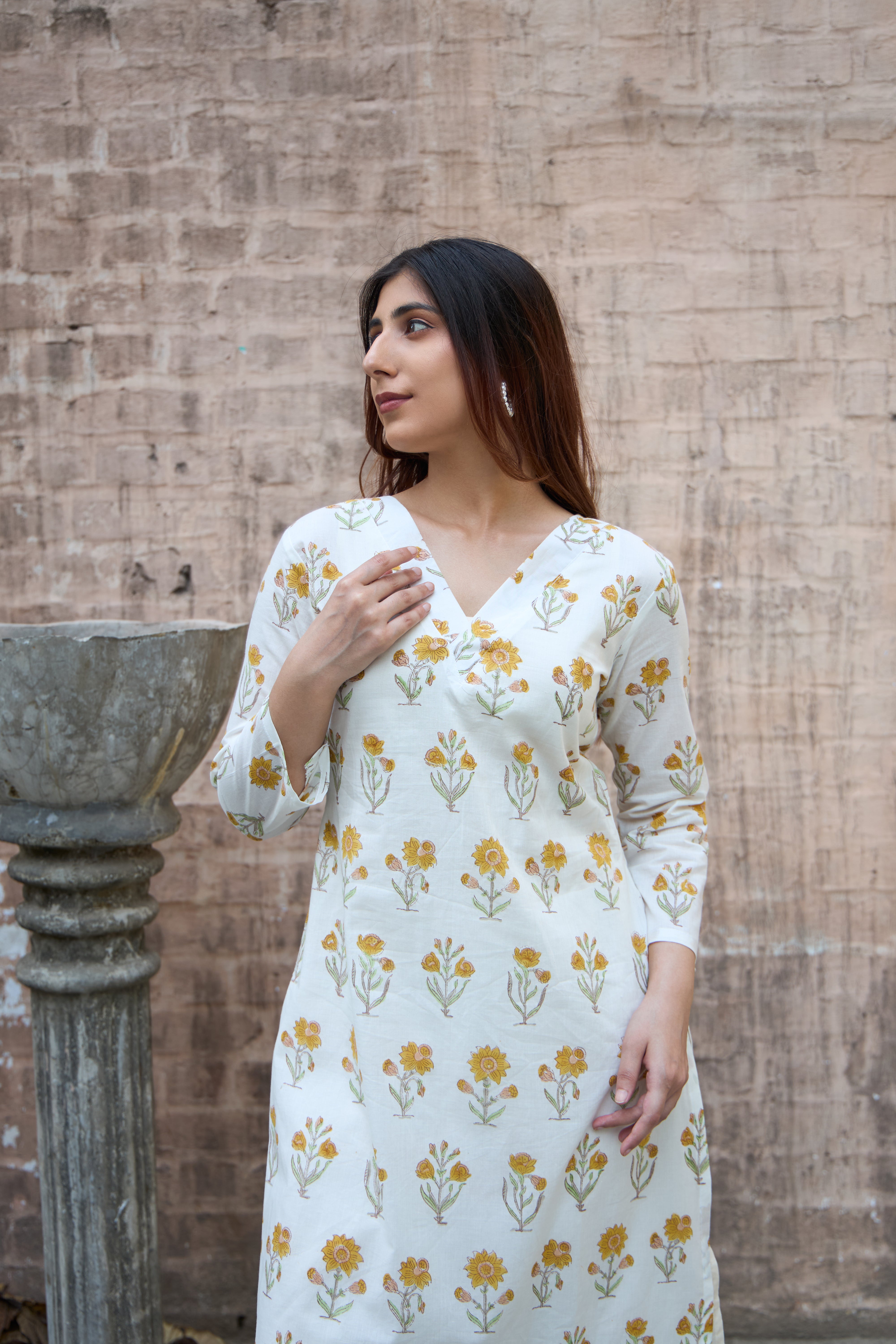 Woman wearing a floral dress standing against a textured wall.