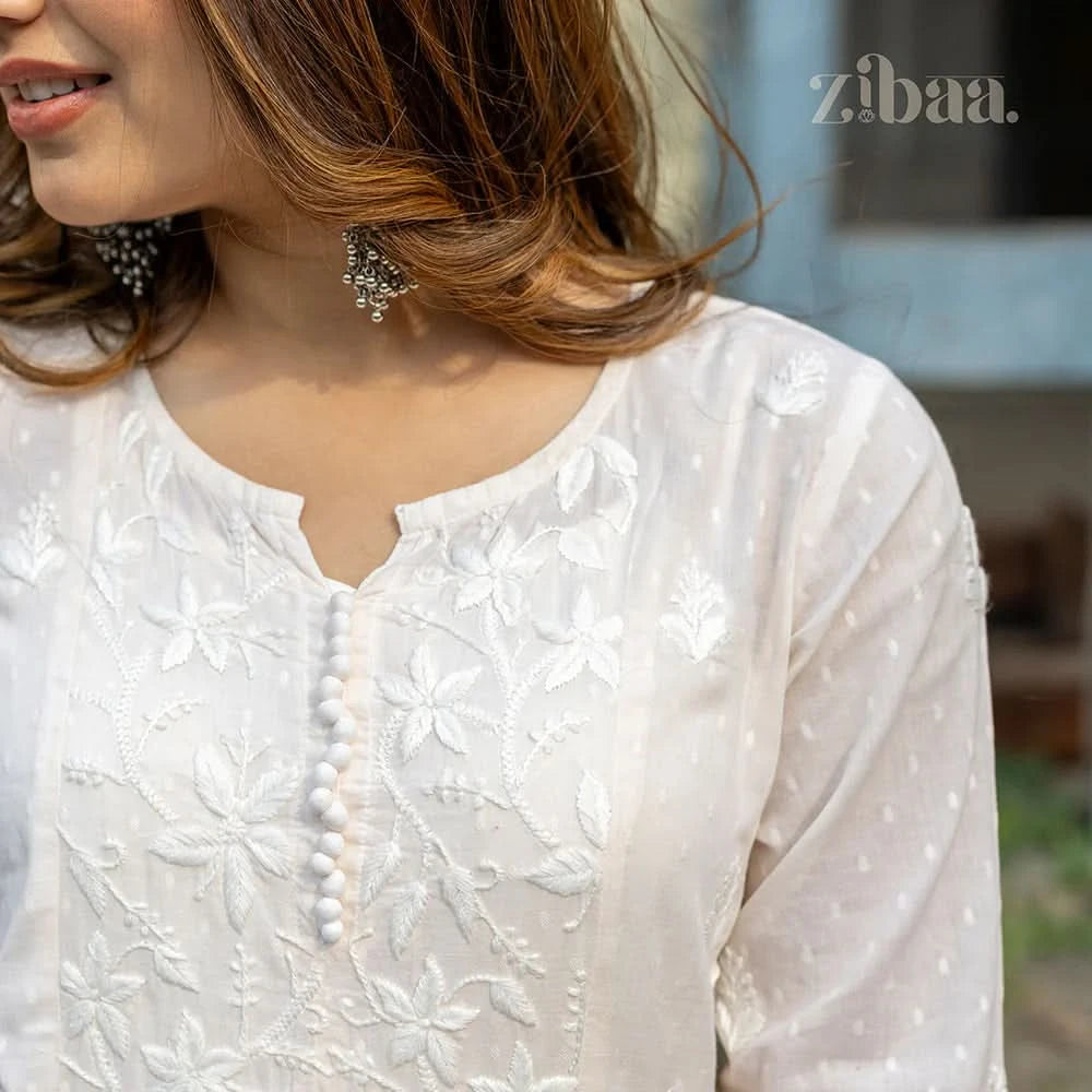 Woman wearing a white embroidered top with a blurred background