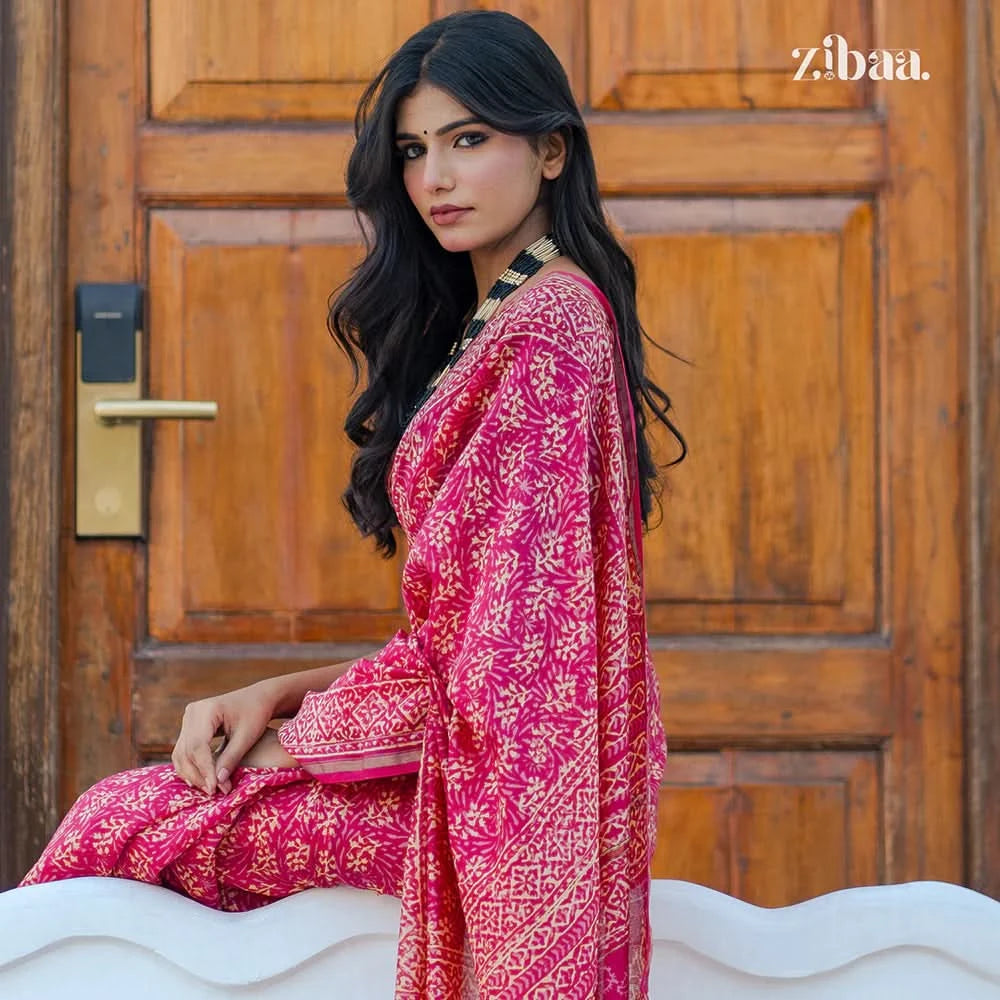 Woman in a pink traditional outfit sitting in front of a wooden door with 'zibaa' branding.