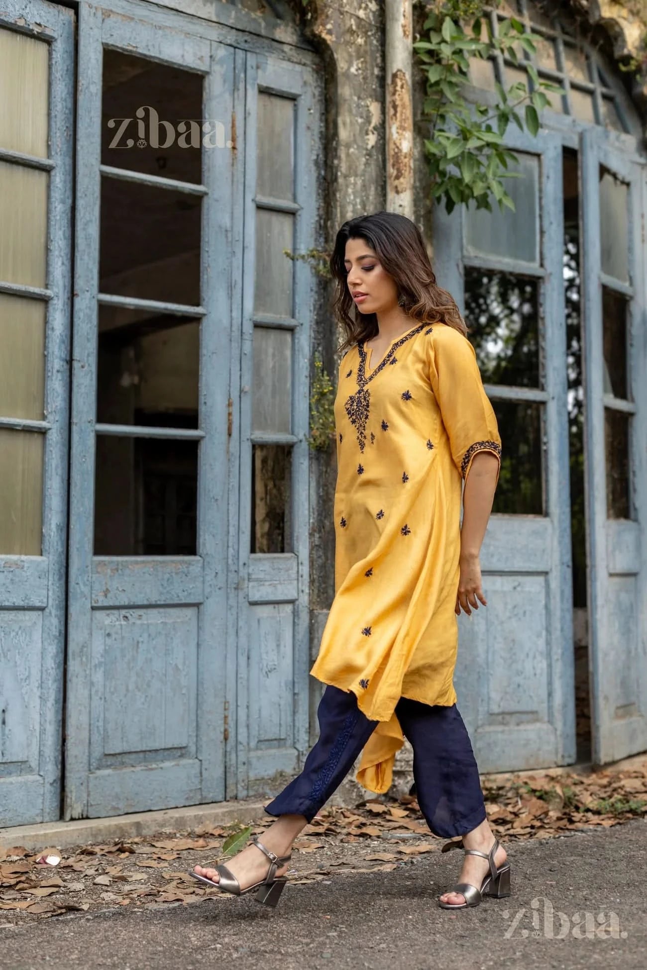 A girl walks wearing a mustard Chikankari Kurta Set paired with navy pants, showcasing elegance and intricate embroidery.