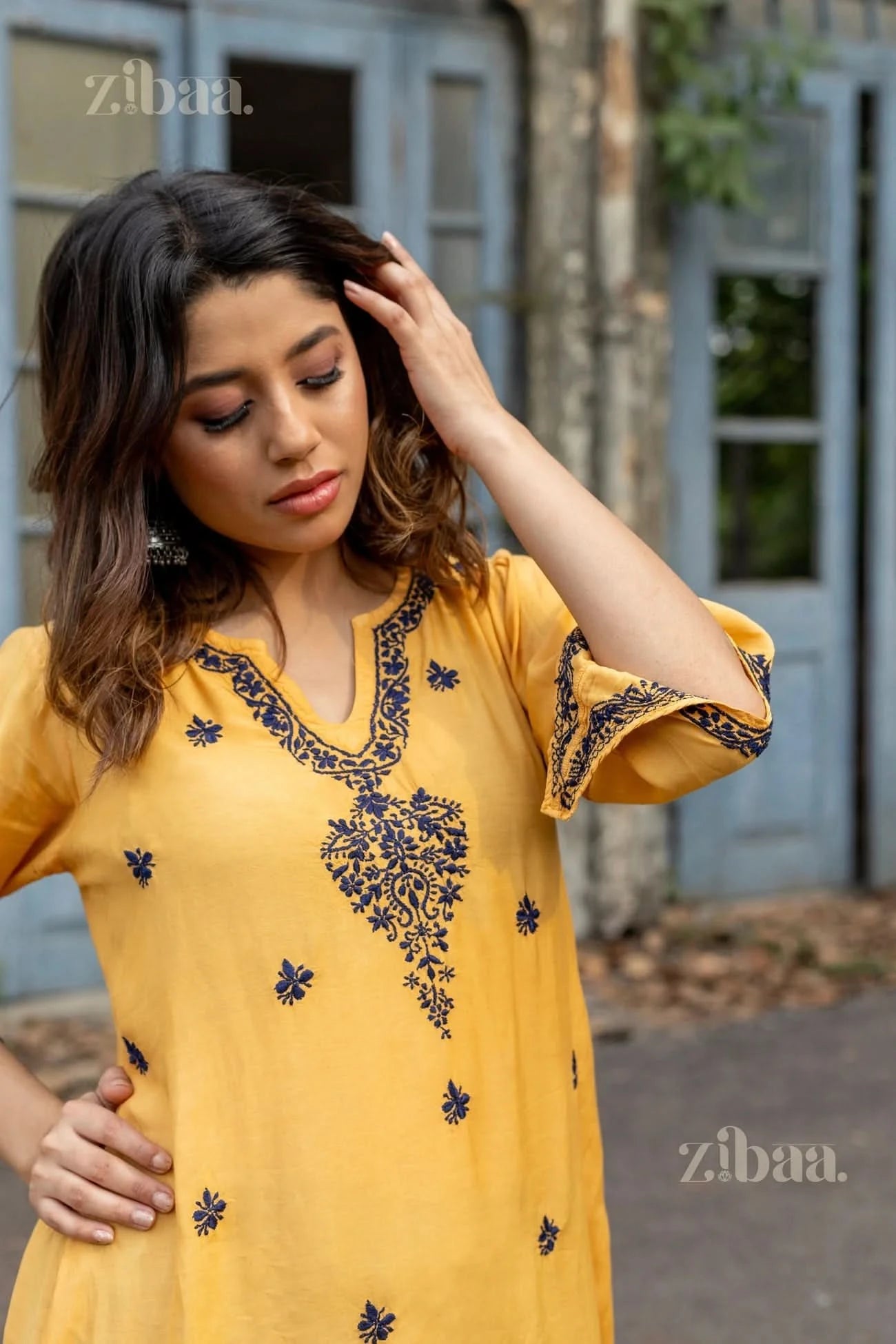 A woman poses in a beautiful mustard Chikankari Kurta Set adorned with intricate navy embroidery, exuding elegance and traditional charm.