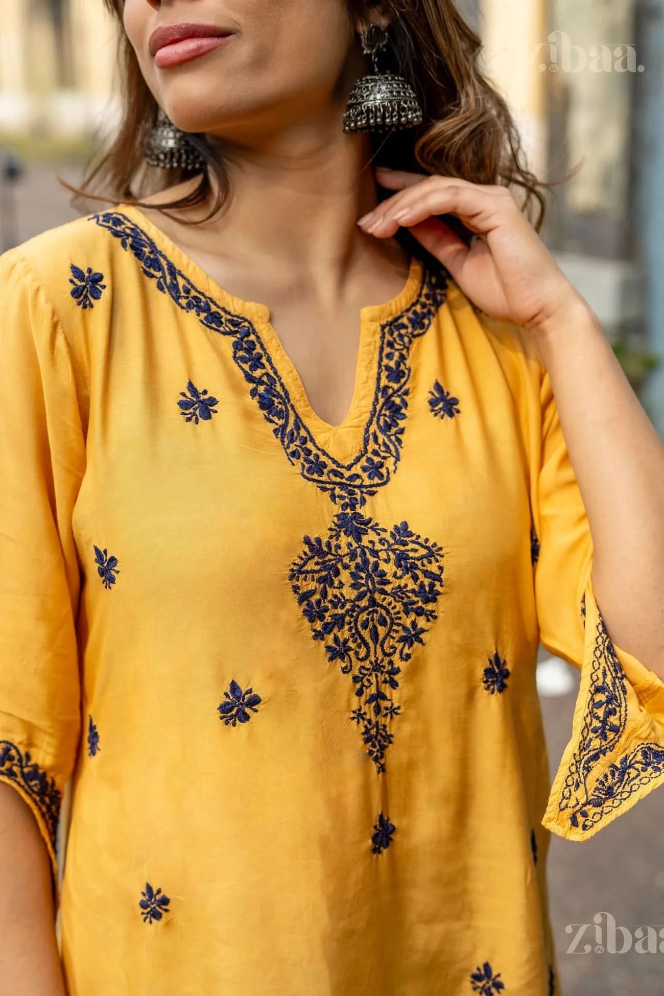 A detailed view of a mustard Chikankari Kurta Set showing navy embroidery on the neckline and sleeves, paired with elegant accessories.