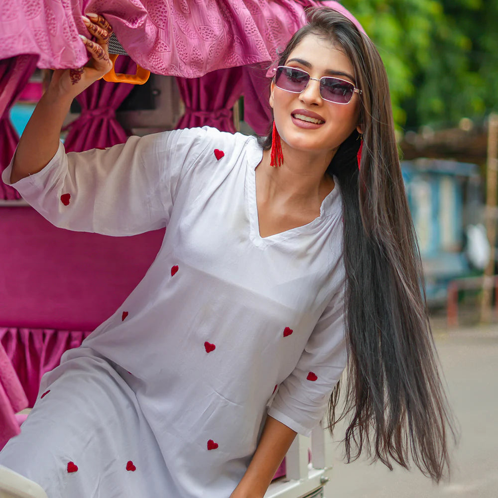 Woman in a white outfit with red heart patterns sitting outdoors