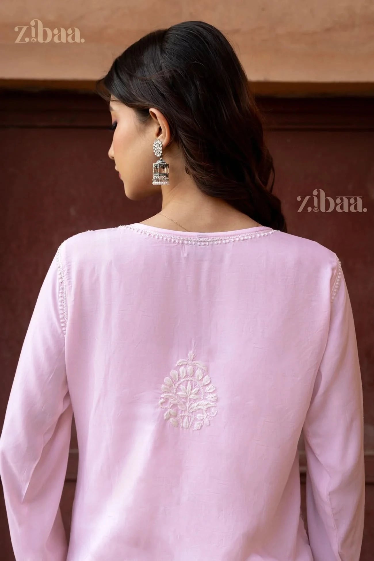 Back view of a pastel pink Kurti featuring delicate white embroidery, paired along with statement earrings for a refined look
