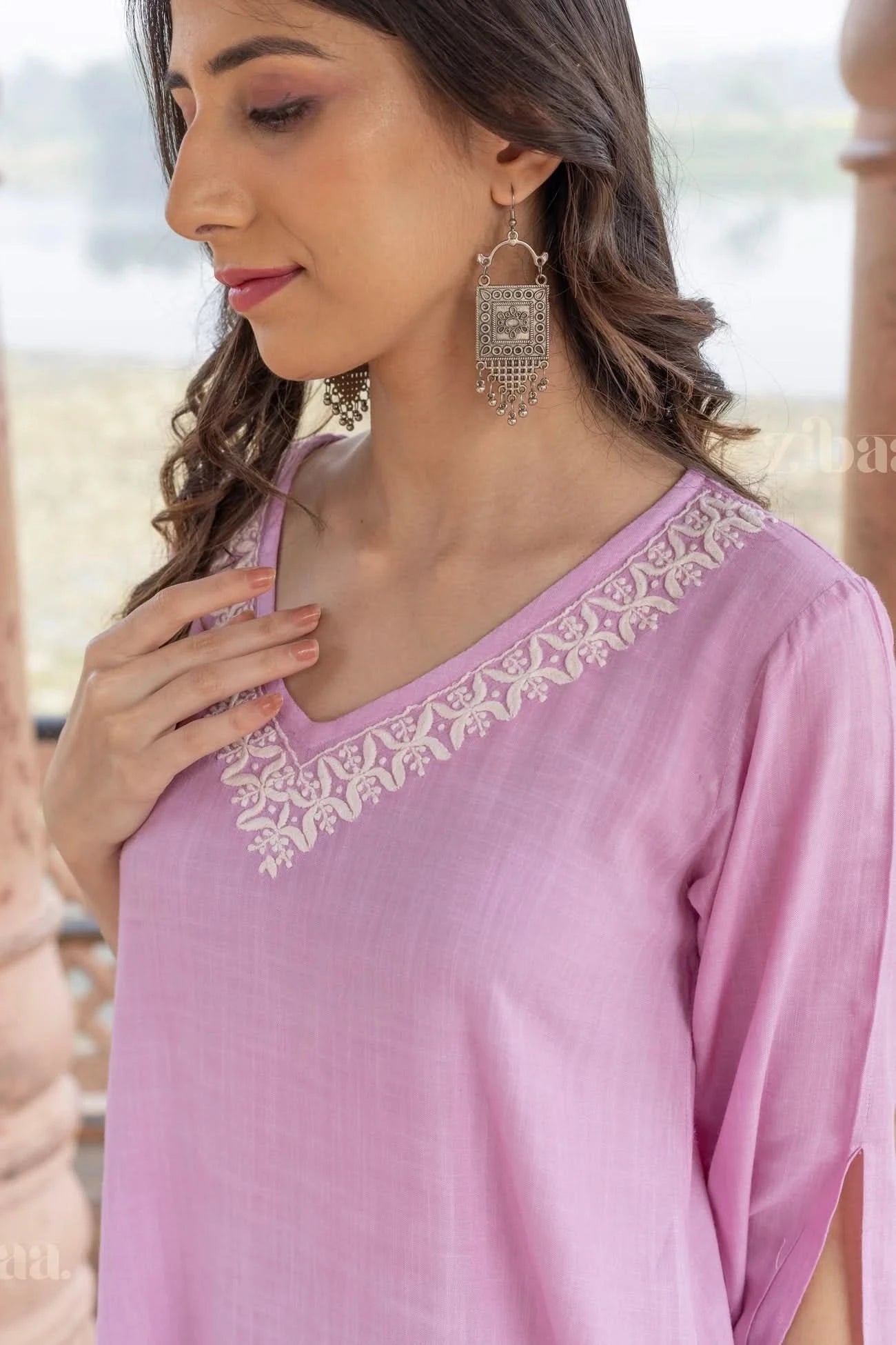 Close-up of a woman wearing a pastel pink Chikankari Kurta Set with delicate embroidery on the neckline, gently touching her neckline