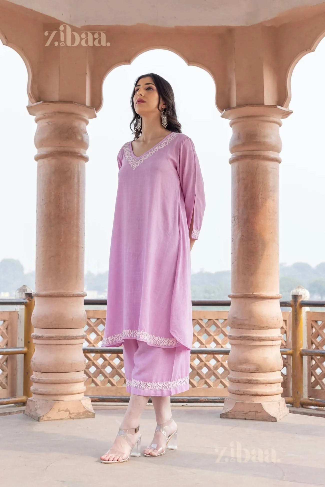 Woman posing confidently in a pastel pink Chikankari Kurta Set with delicate embroidery, standing outdoors under an ornate pavilion