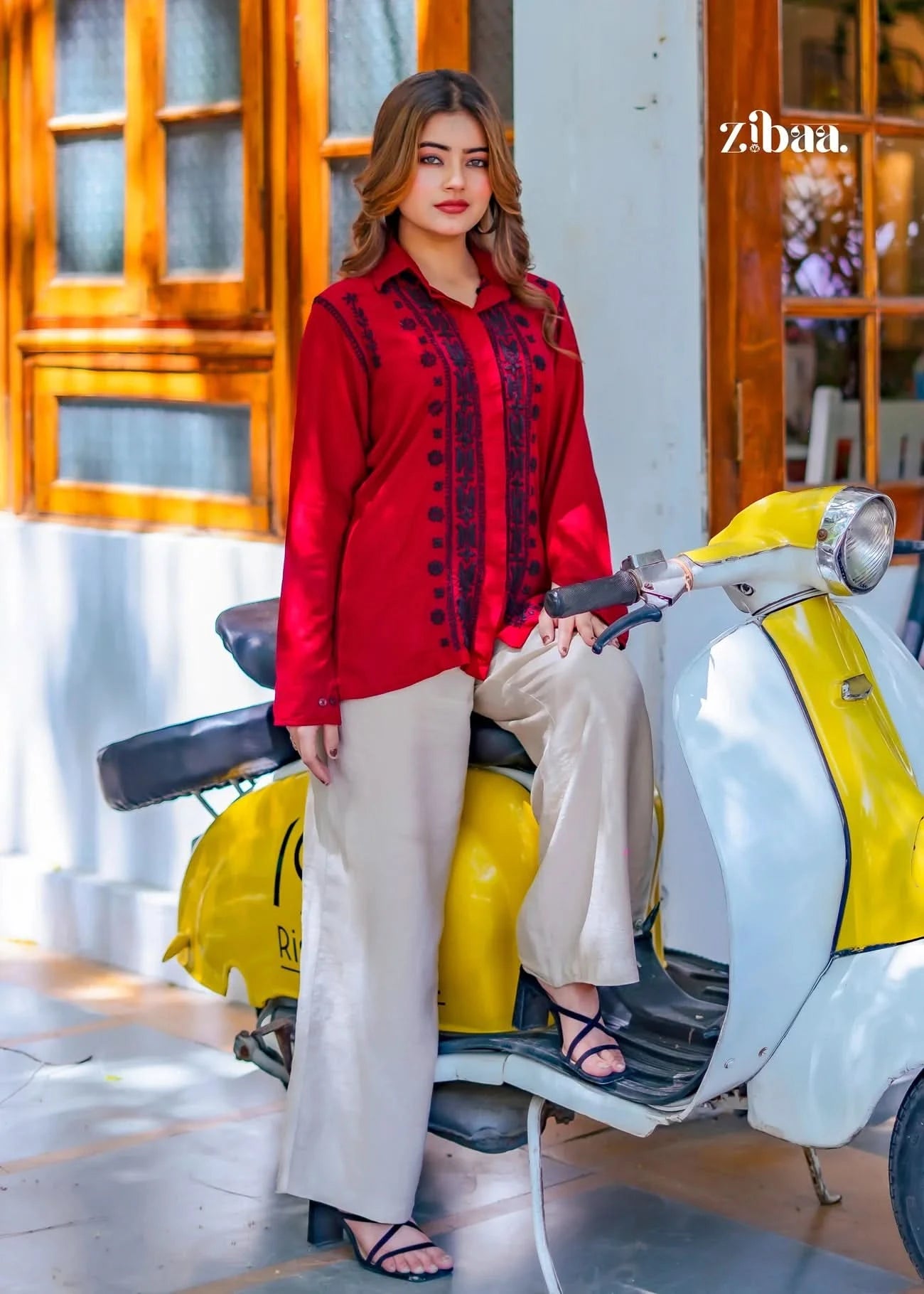 The model stands outdoors, confidently posing on a scooter while wearing a red chikankari shirt with intricate black embroidery.