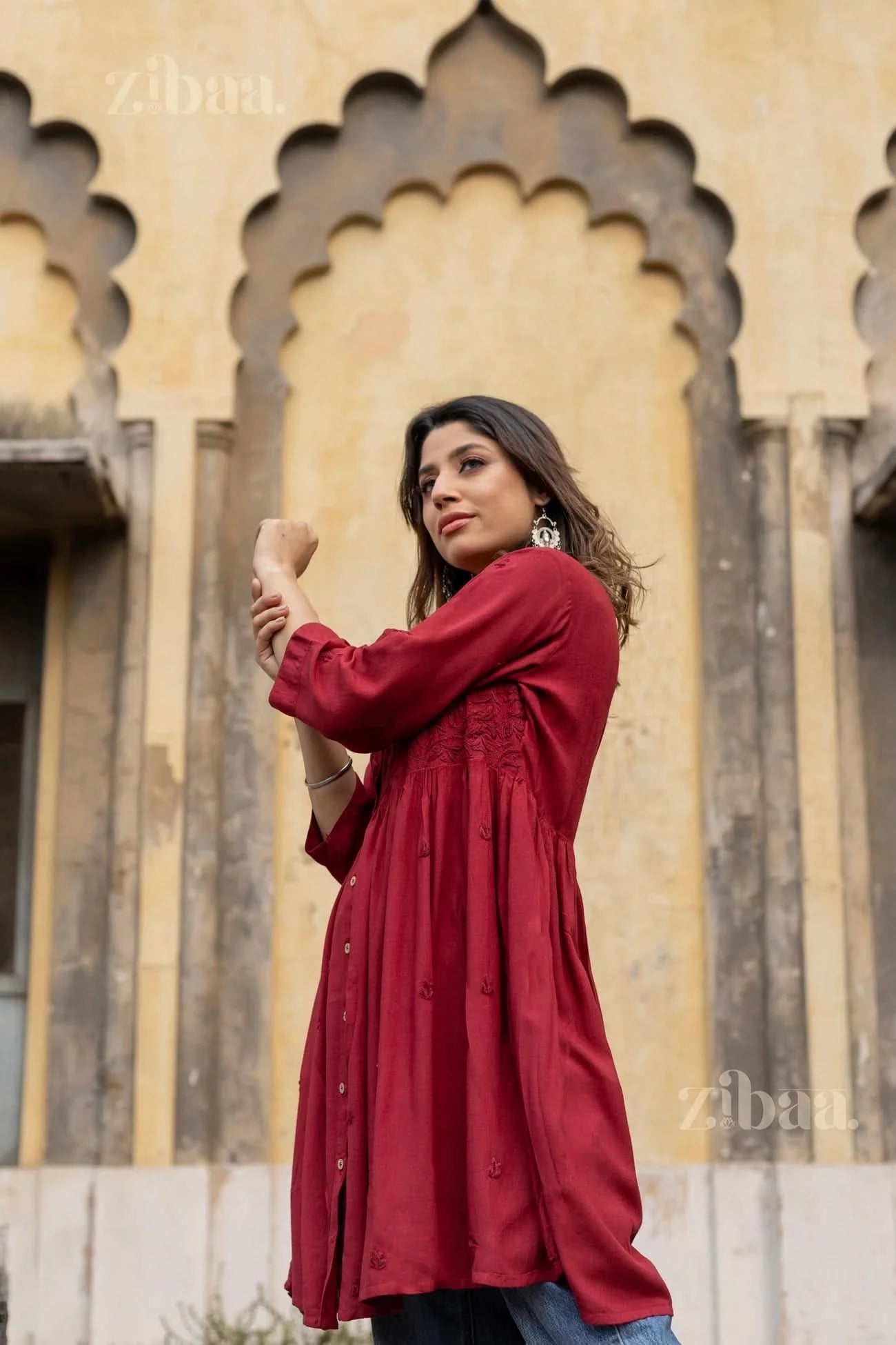 A woman adjusts her sleeve while posing outdoors in a maroon rayon Chikankari top, showcasing its flowy design and tonal embroidery.