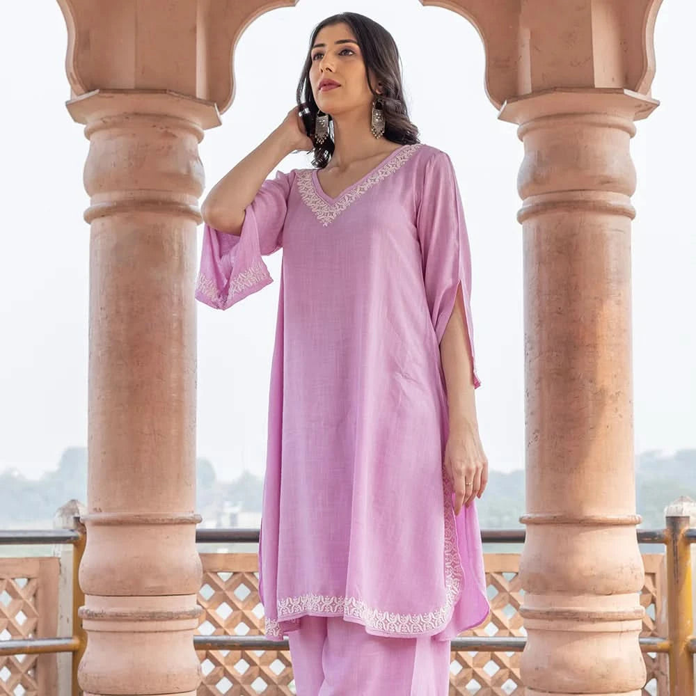 Woman in a pink traditional outfit standing between stone columns with a blurred scenic background