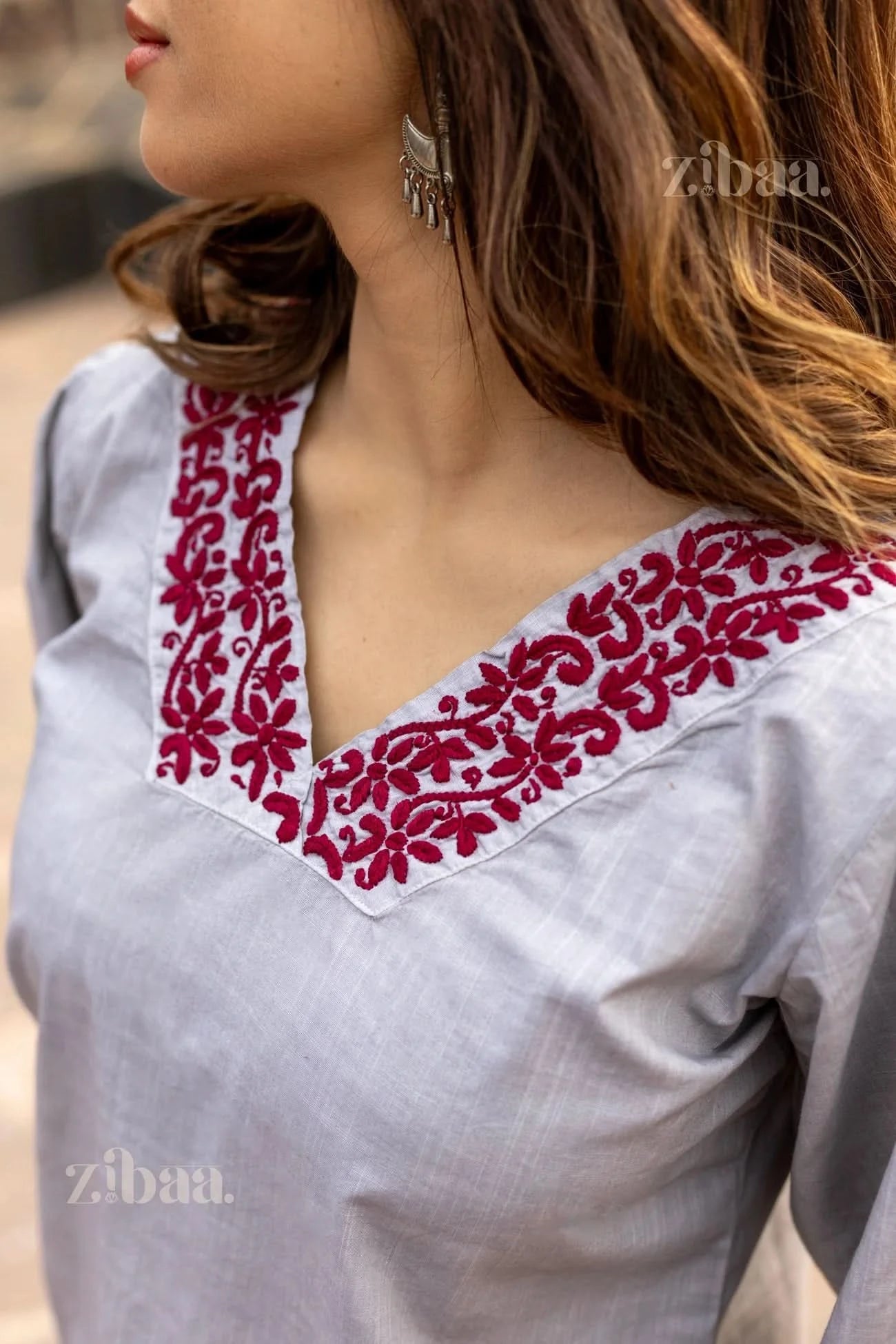 Close-up of a woman wearing a grey Chikankari top, showing red floral embroidery on the V-neckline, paired with silver earrings